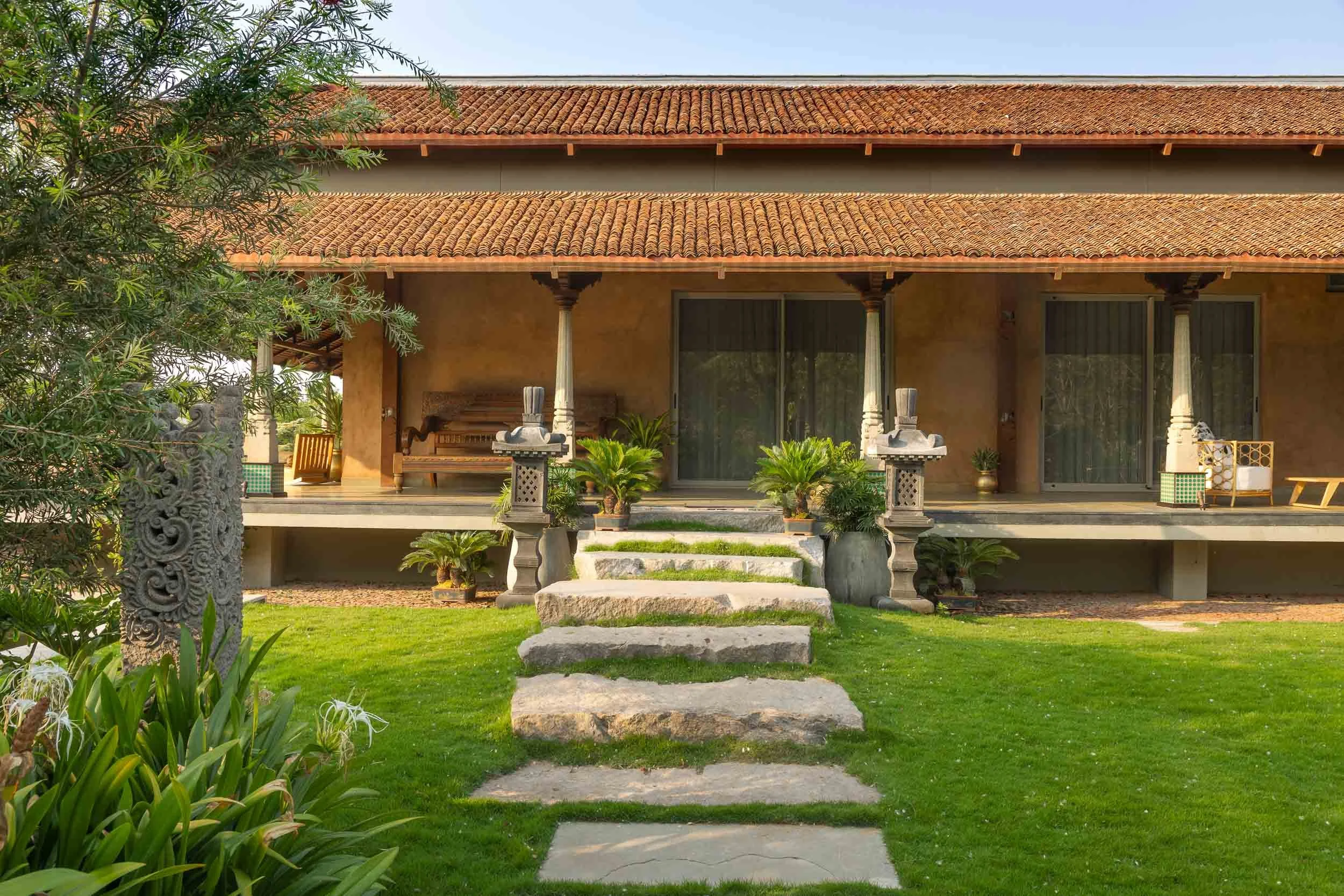Wide exterior daytime photography of a luxury resort farm stay featuring an expansive manicured green lawn, mature trees, and a traditional pitched-roof building in the background.