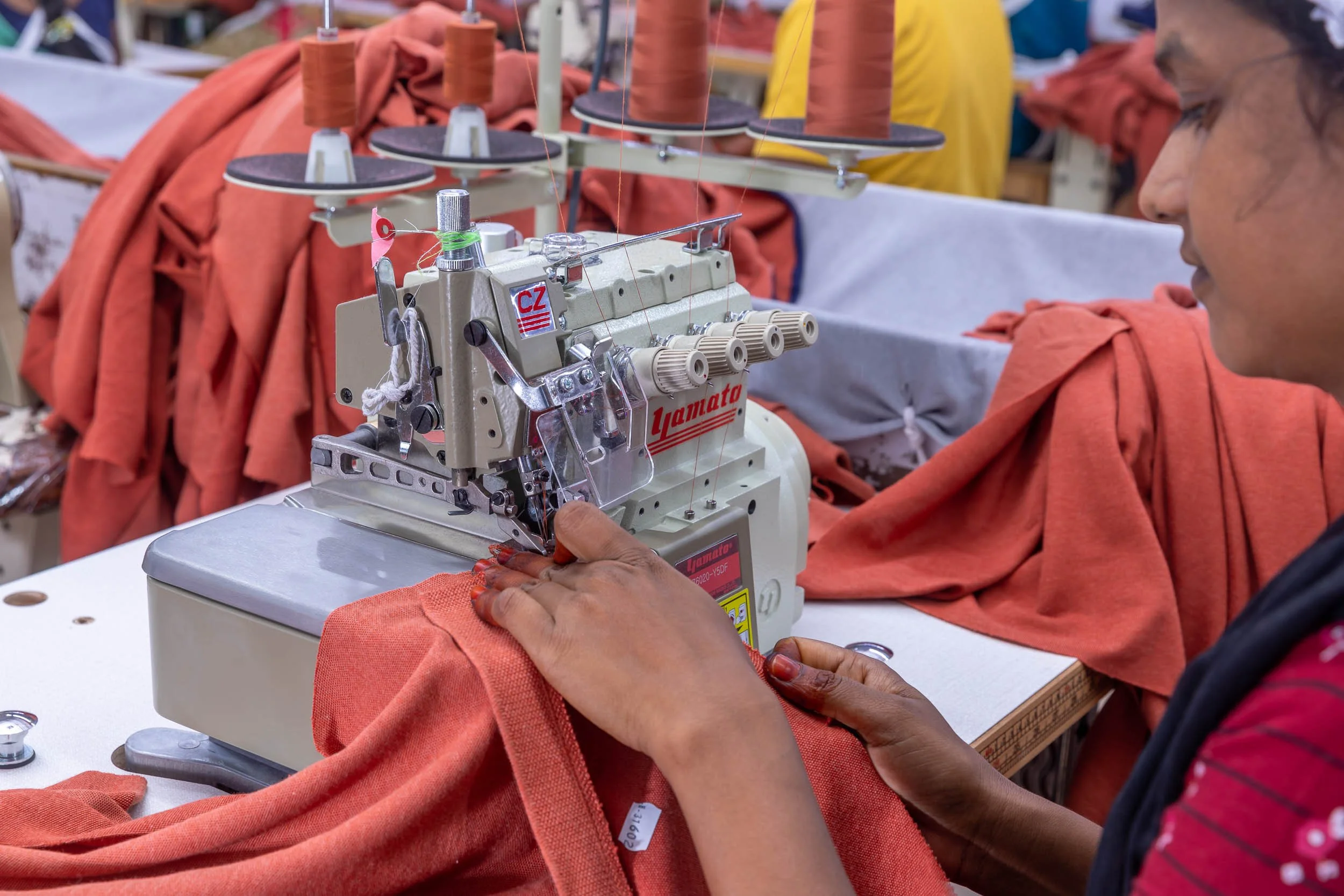 Close-up industrial photography of a textile worker's hands operating specialized garment machinery on vibrant red fabric.