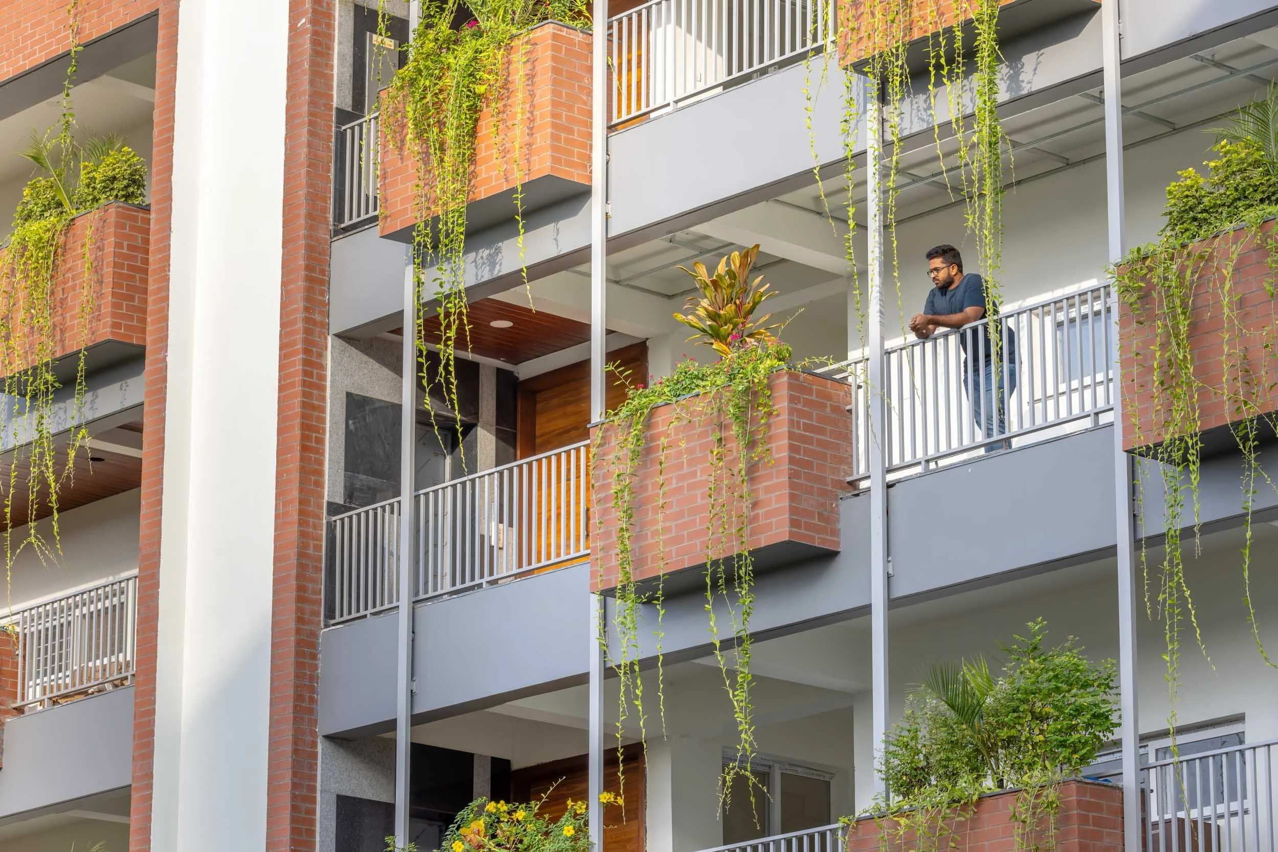 Professional architectural photography capturing a modern multi-story exterior, highlighting biophilic design elements with lush trailing balcony plants, warm wood paneling, and an integrated lifestyle element