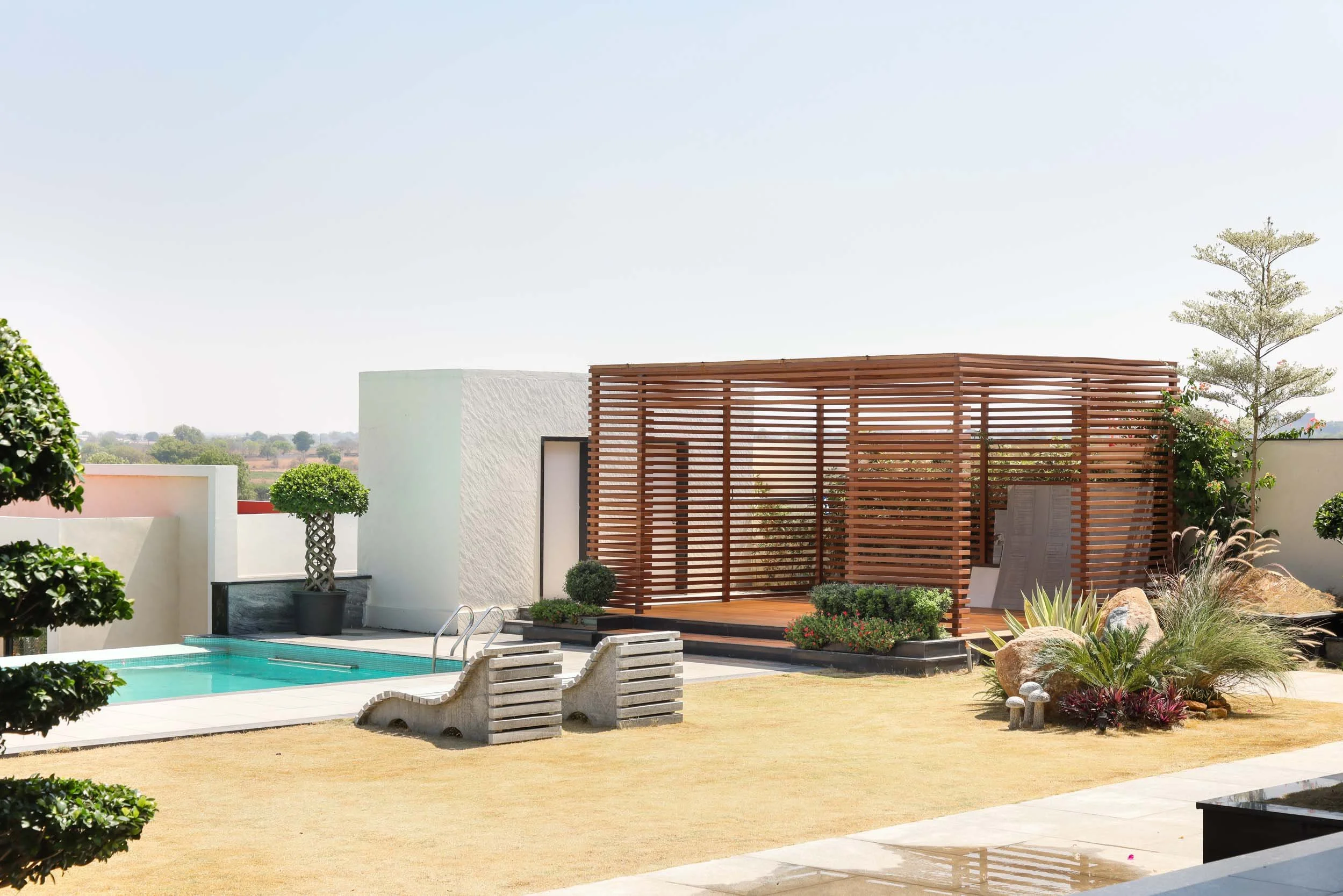 Professional exterior architectural photography of a luxury residential pool area, highlighting a modern wooden cabana and pristine landscaping