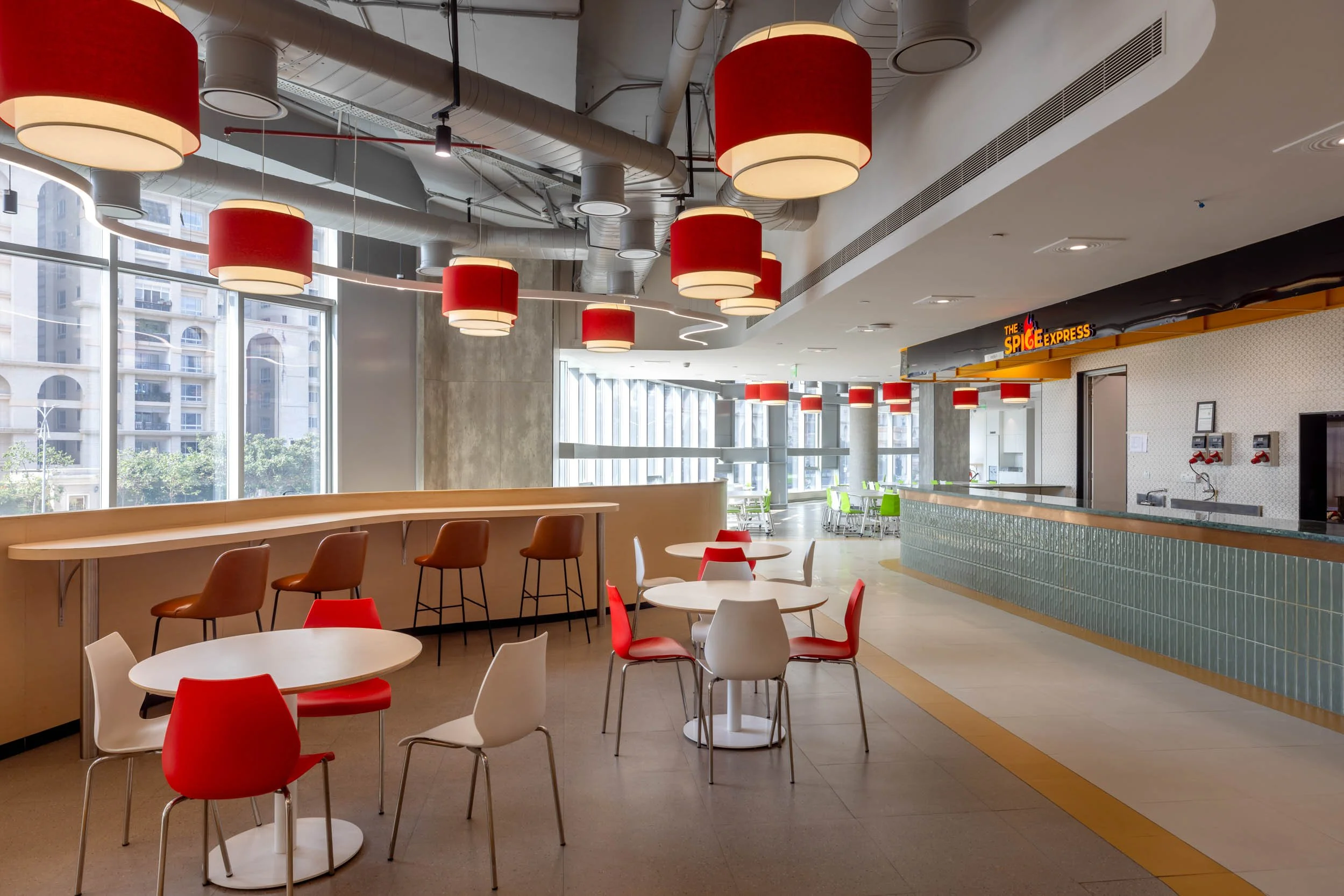 Commercial interior photography showcasing a modern cafeteria design, highlighting vibrant red pendant lighting, exposed ceiling architecture, and bright casual dining interiors