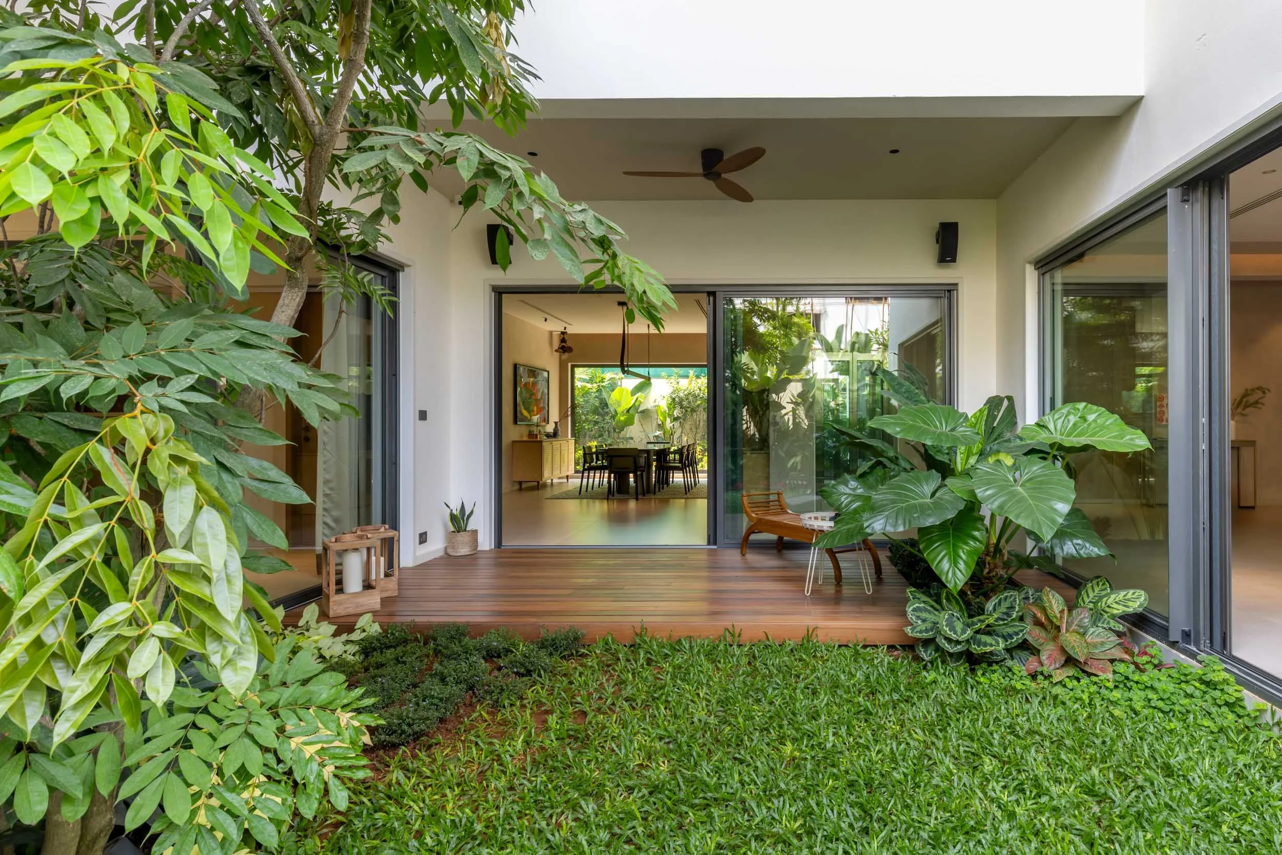 View from a covered wooden patio through wide open sliding glass doors into a vibrant green courtyard garden