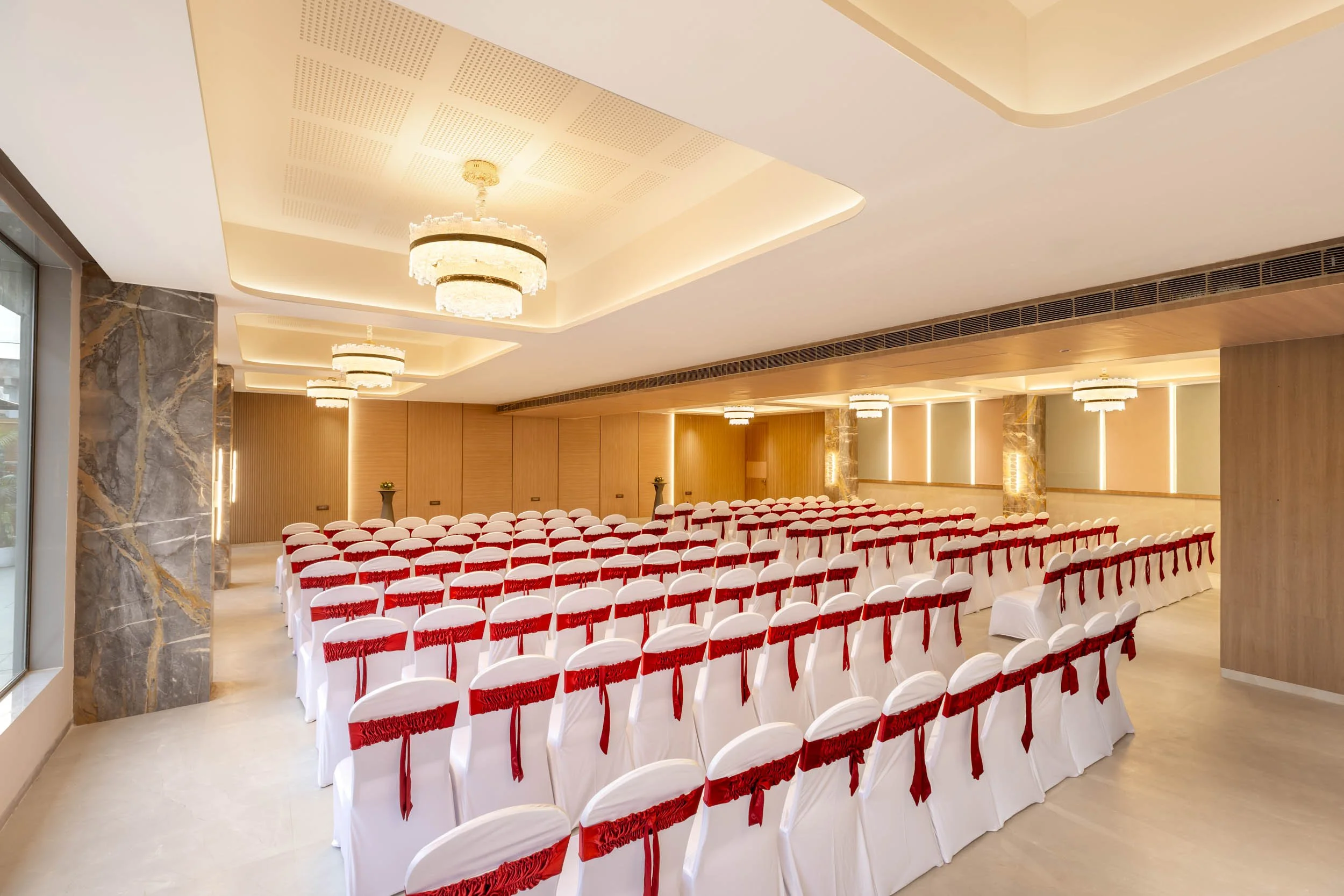 Interior photography of a spacious hotel conference hall set up with theater-style seating, featuring red and white chairs, and a warm tray ceiling with ambient lighting