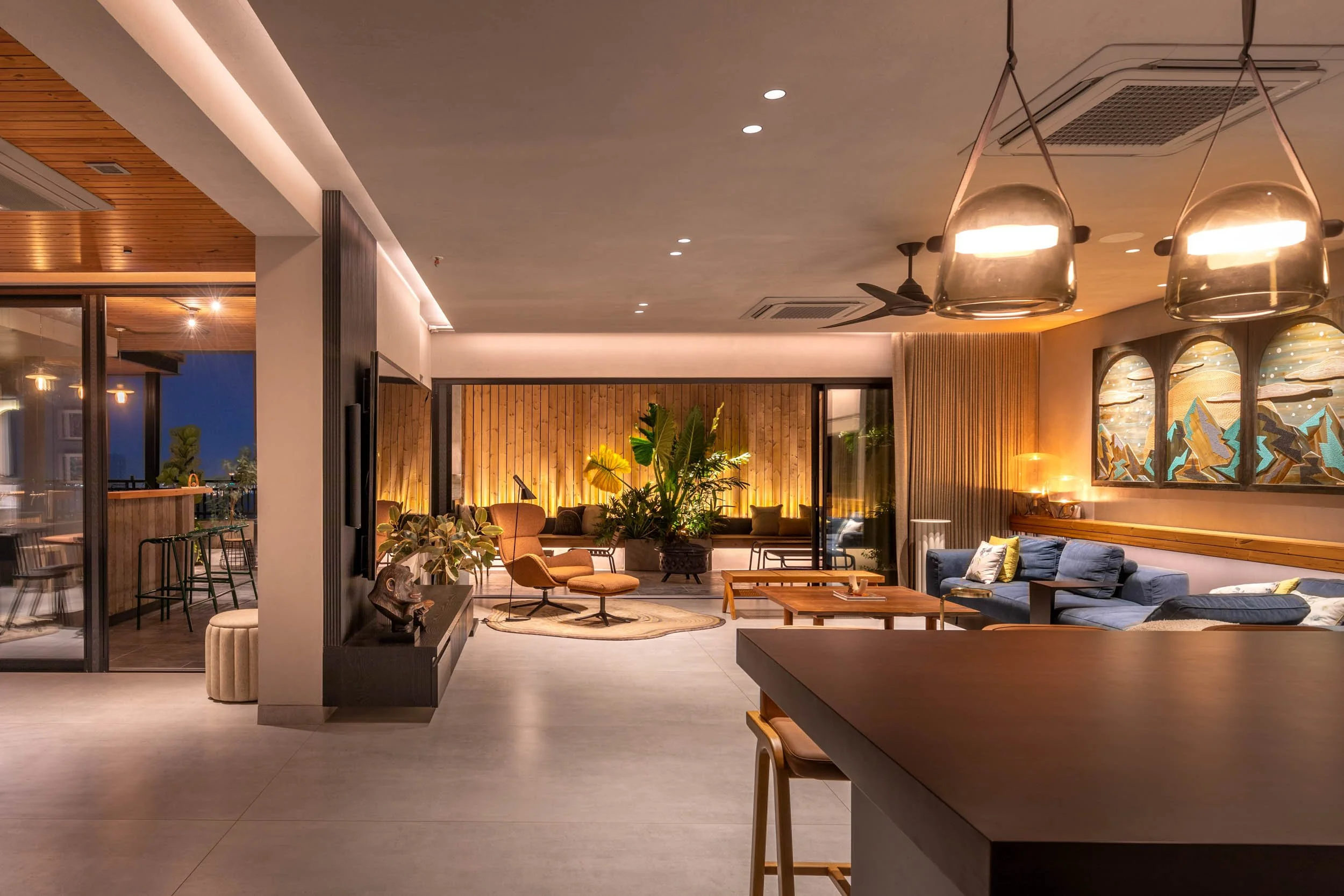 Wide interior photography of a spacious modern living room at twilight, featuring layered architectural lighting, contemporary seating, and warm wooden flooring