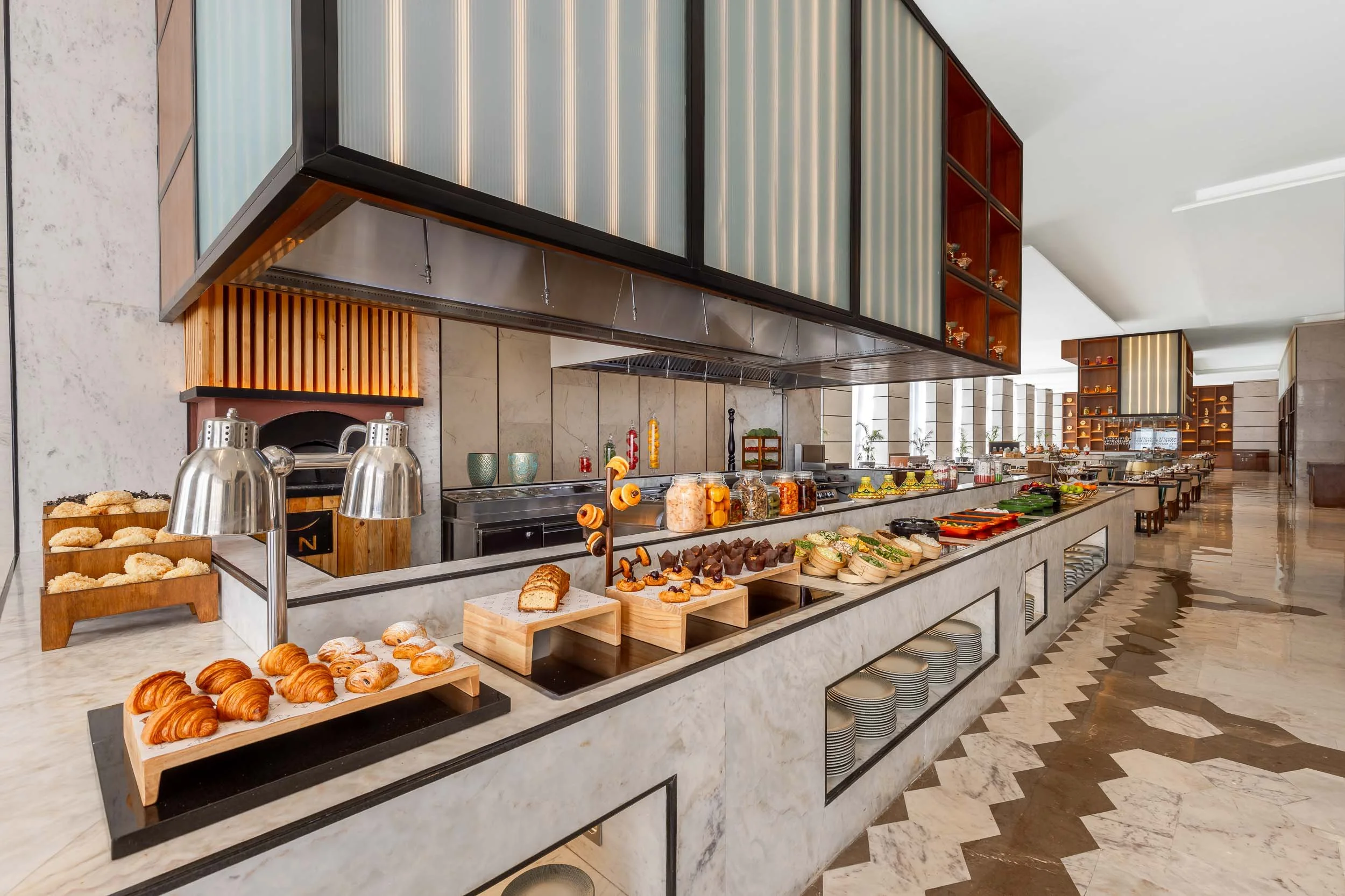 nterior photography of a modern hotel breakfast buffet station featuring a long serving counter, food displays, and a distinctive custom slatted overhead canopy