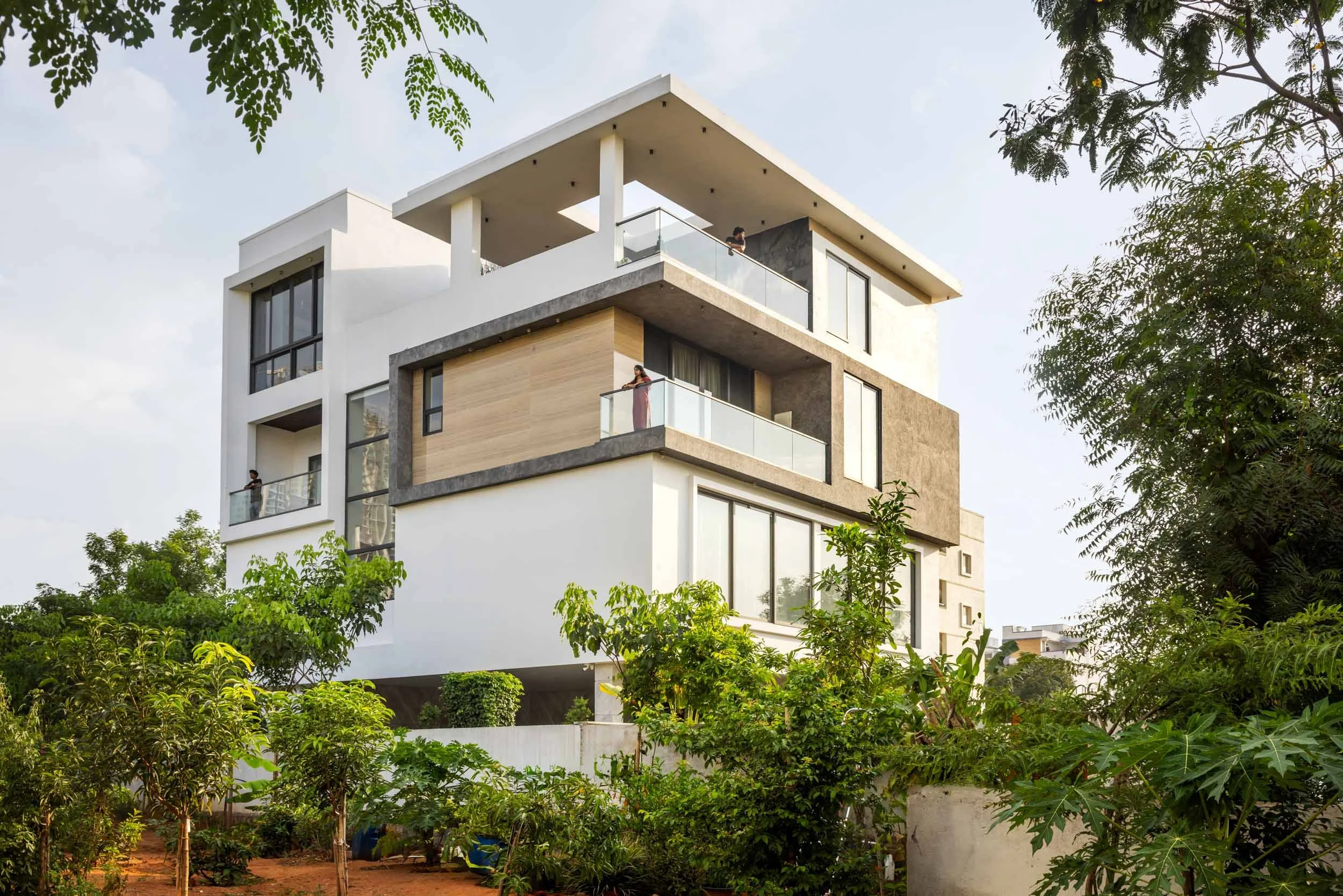 Professional exterior architectural photography of a modern multi-story residential home, highlighting a clean white geometric facade and distinctive wooden balcony louvers.