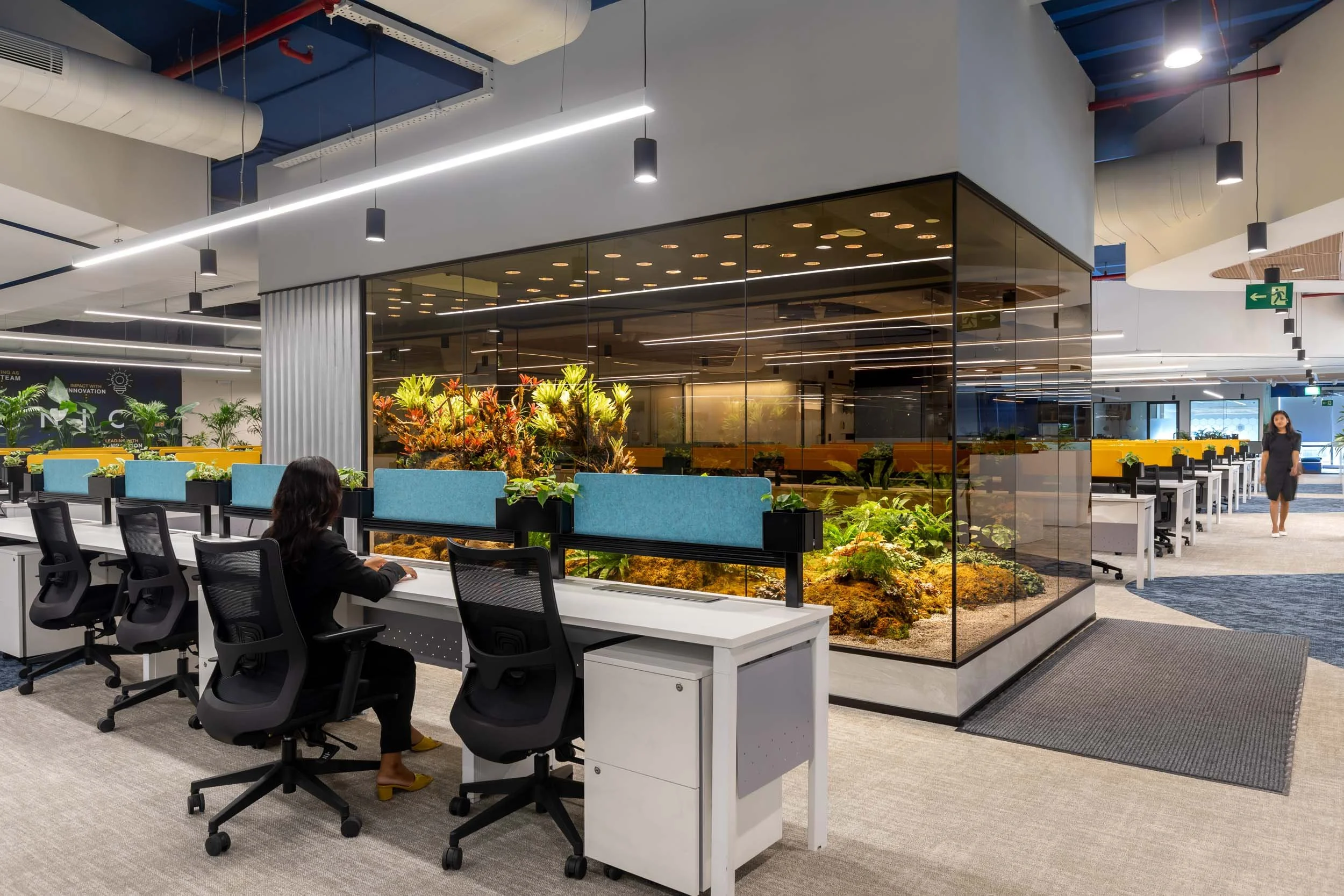 Commercial interior photography showcasing a modern corporate workspace, highlighting open-plan desk arrangements, a raised collaborative meeting zone with acoustic partitions, and biophilic design elements.