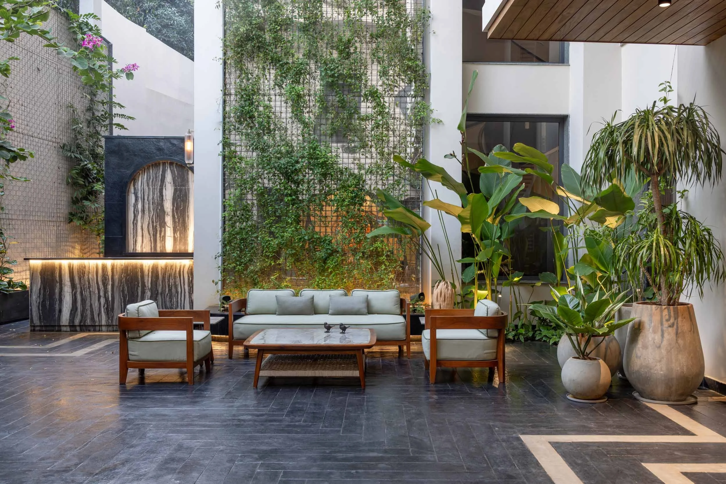 Contemporary outdoor courtyard patio featuring modern wooden lounge furniture, dark tile flooring, and a lush vertical garden wall.