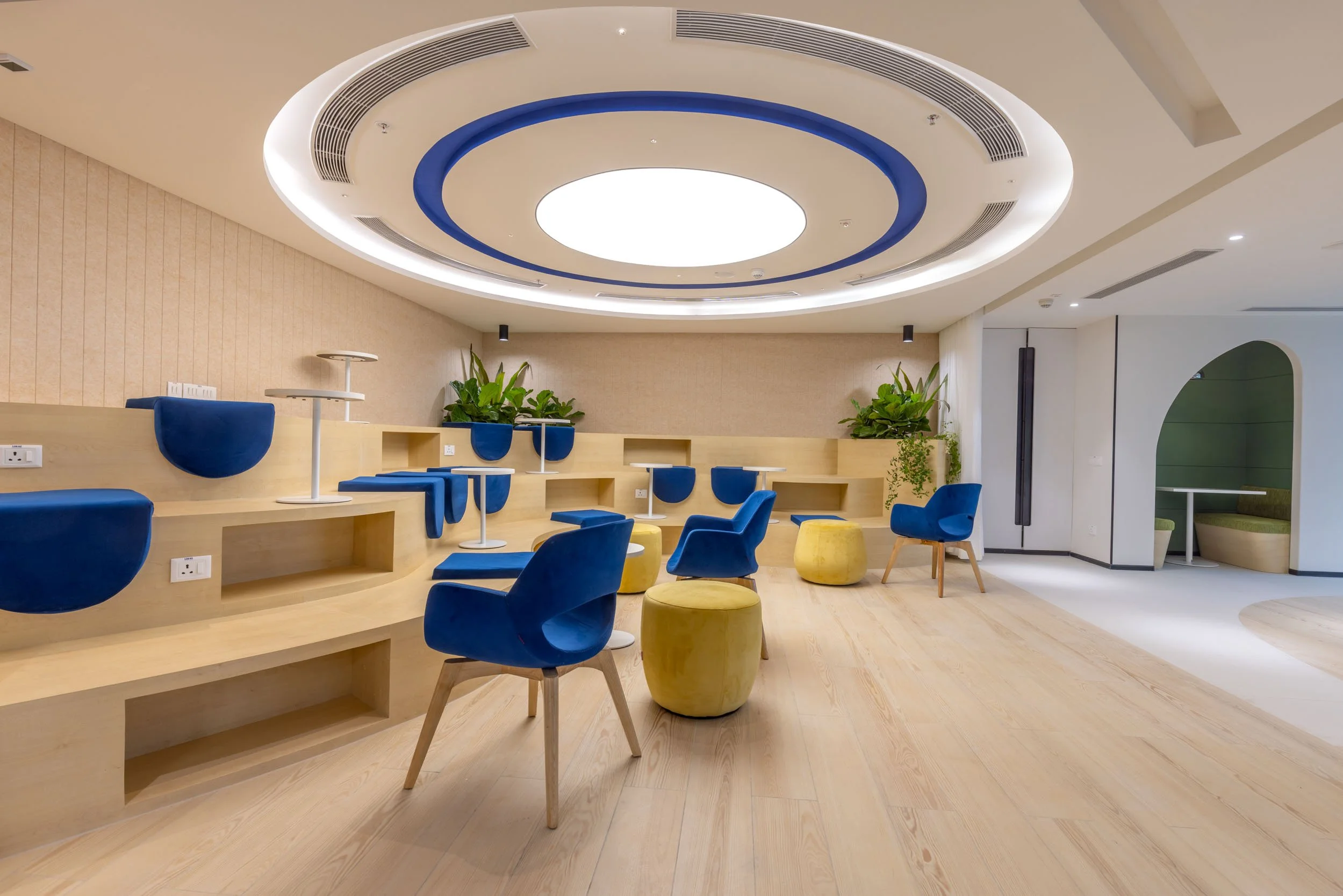 Commercial interior photography showcasing a modern collaborative presentation space, highlighting custom tiered wooden seating, circular architectural lighting, and vibrant corporate furniture