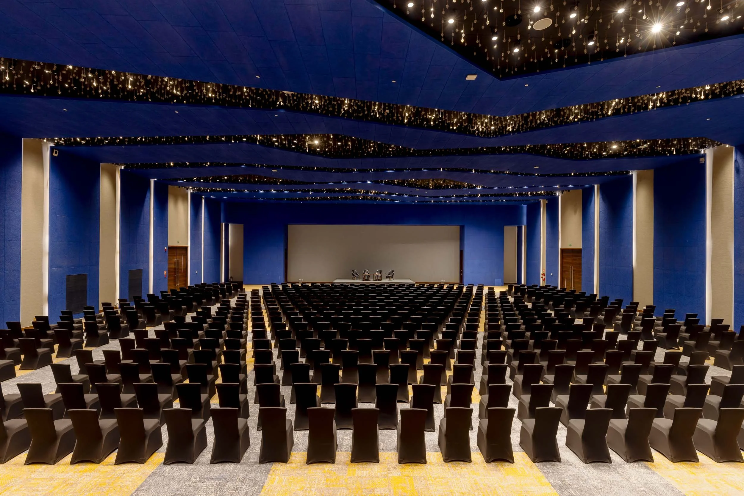 Interior photography of a large hotel convention center featuring theater-style seating, blue acoustic wall panels, and a high ceiling with decorative starry lighting