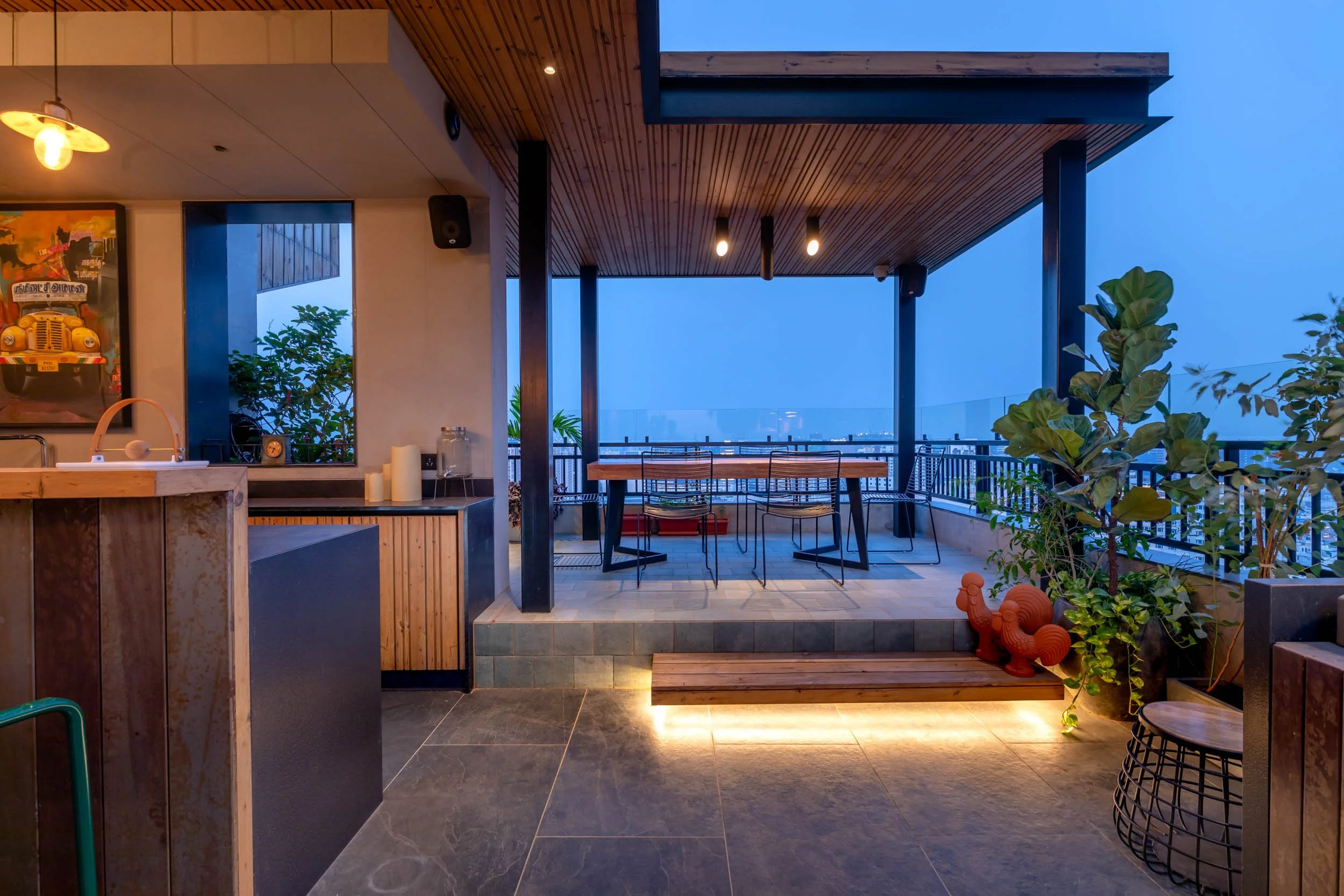 Modern outdoor patio terrace at twilight featuring warm architectural lighting, under-step LED illumination, a dark wooden pergola, and comfortable lounge seating