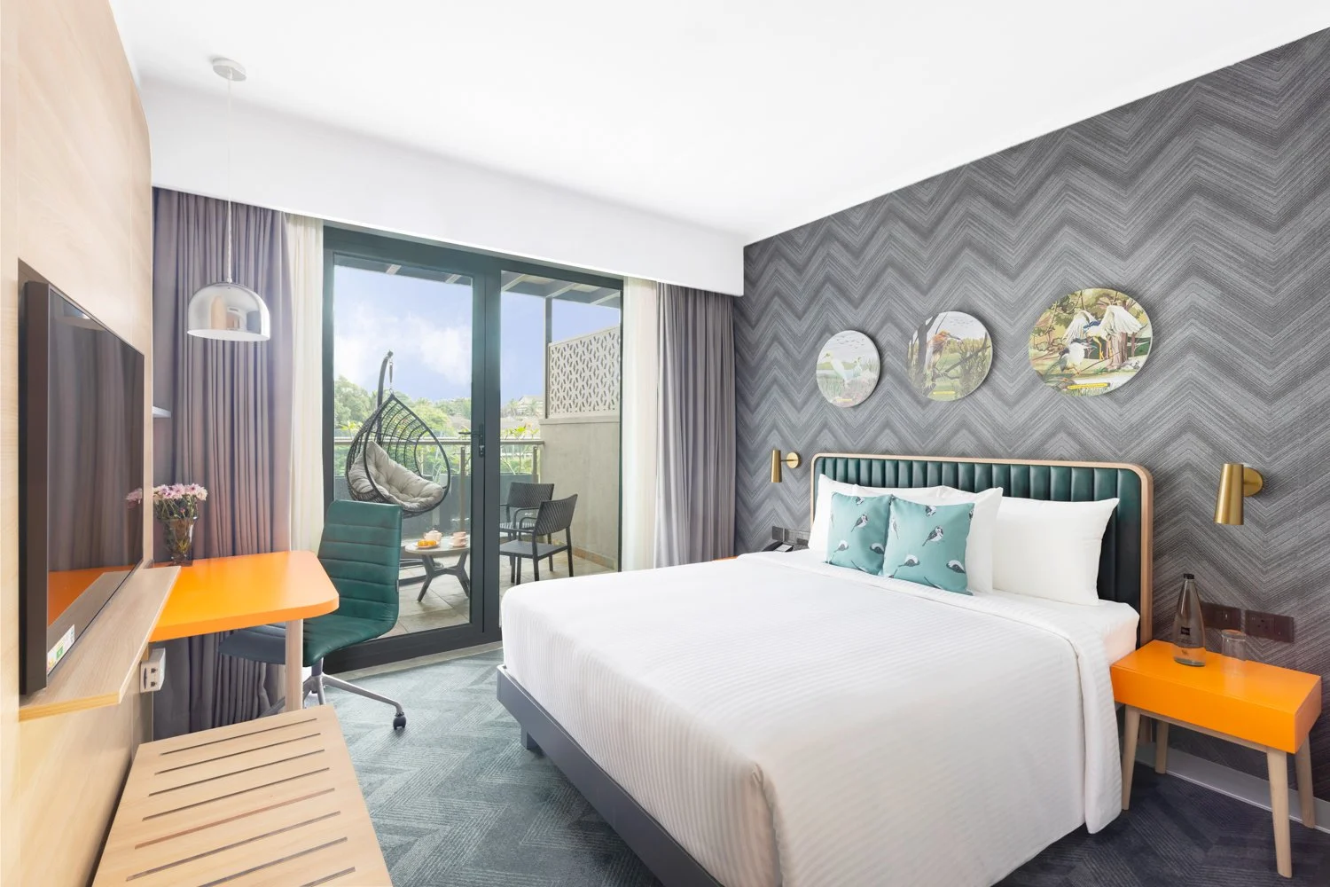Interior photography of a modern hotel bedroom featuring a grey geometric accent wall, a white bed with teal pillows, an orange nightstand, a wall-mounted TV, and a large window