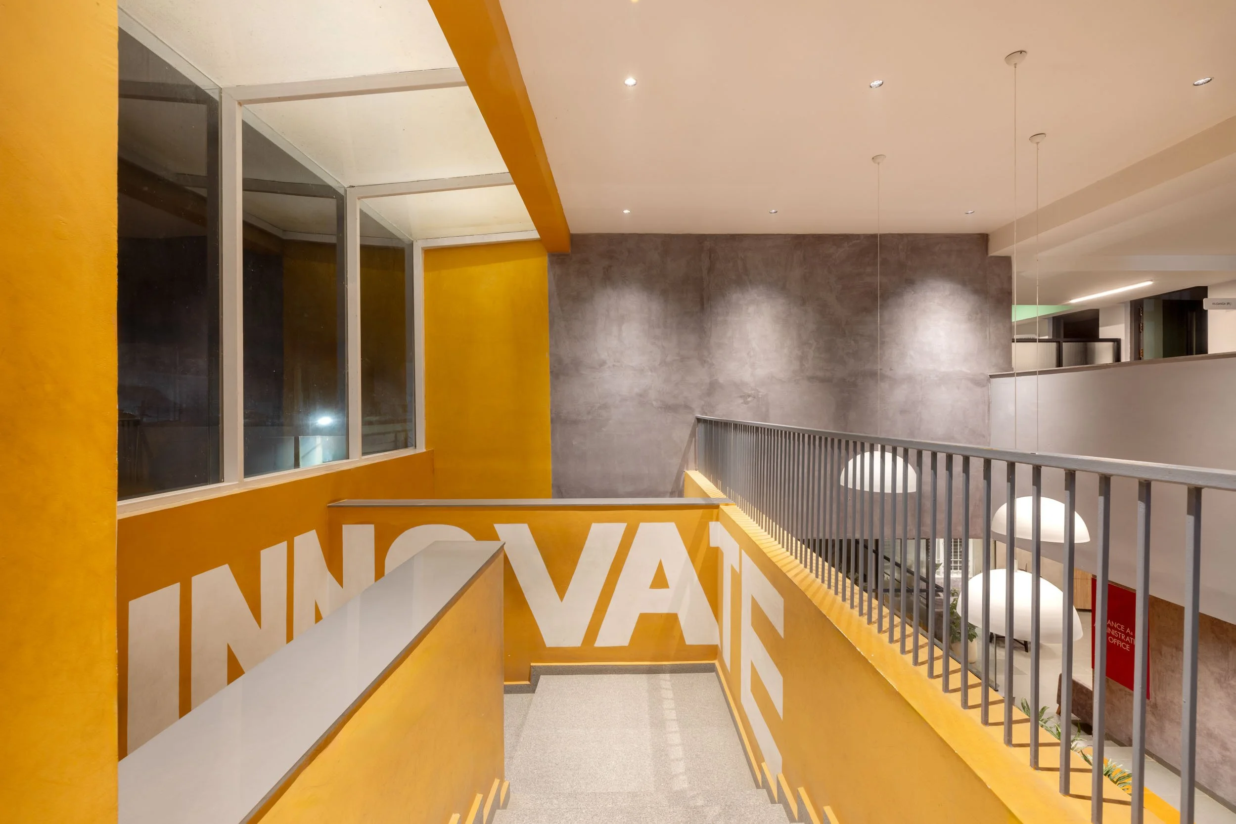 Professional interior architecture photography of a modern commercial or educational space, highlighting dynamic multi-level corridors, vibrant yellow accents, and glass partitions