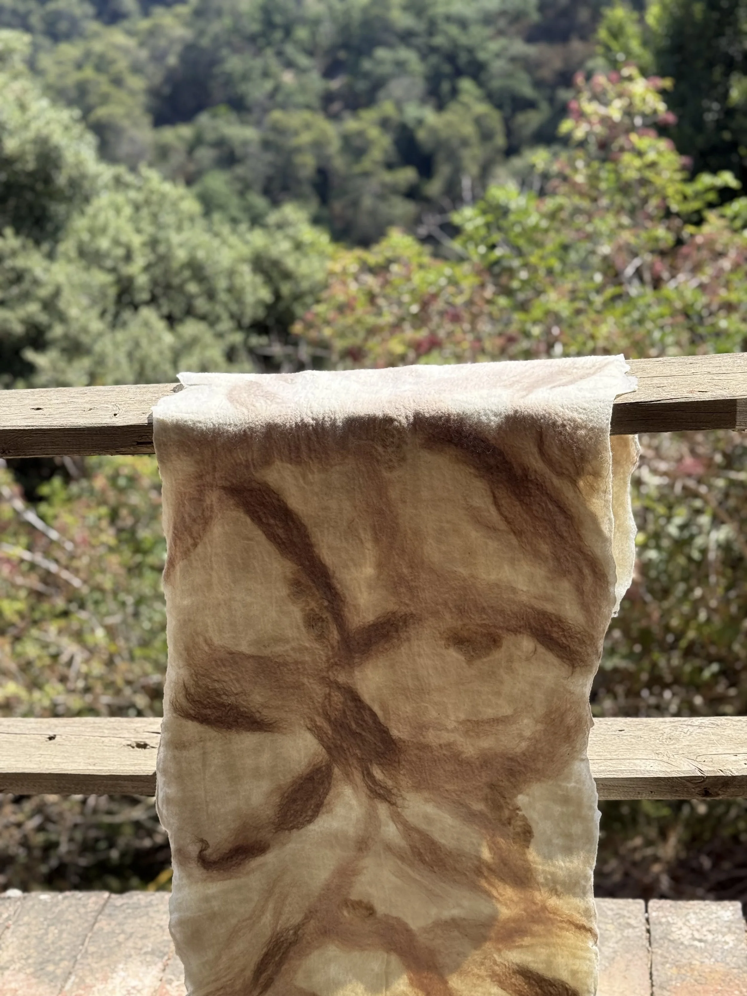 A piece of fabric, possibly resembling animal fur, hanging on a wooden railing outdoors with a blurry green forest background.