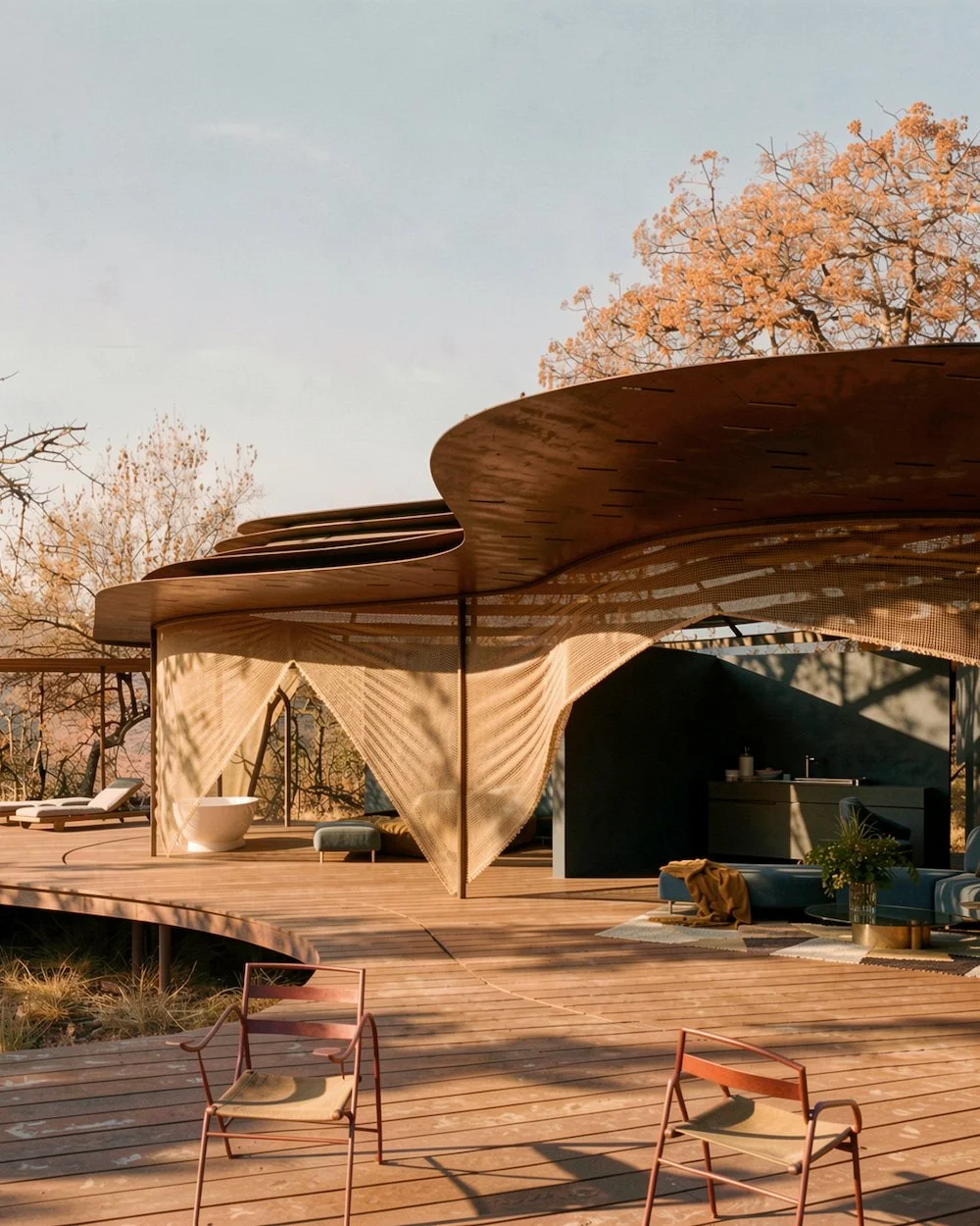 Modern outdoor patio with wooden deck, stylish canopy, lounge chairs, sofa, bathtub, and trees with fall foliage in the background during sunset.