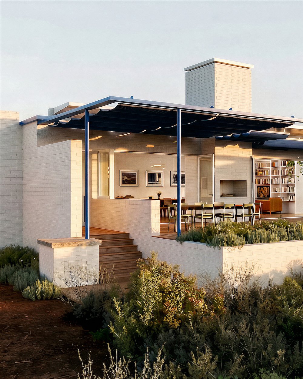 Modern house with a white brick exterior and an outdoor patio with dining table and chairs, surrounded by garden plants.