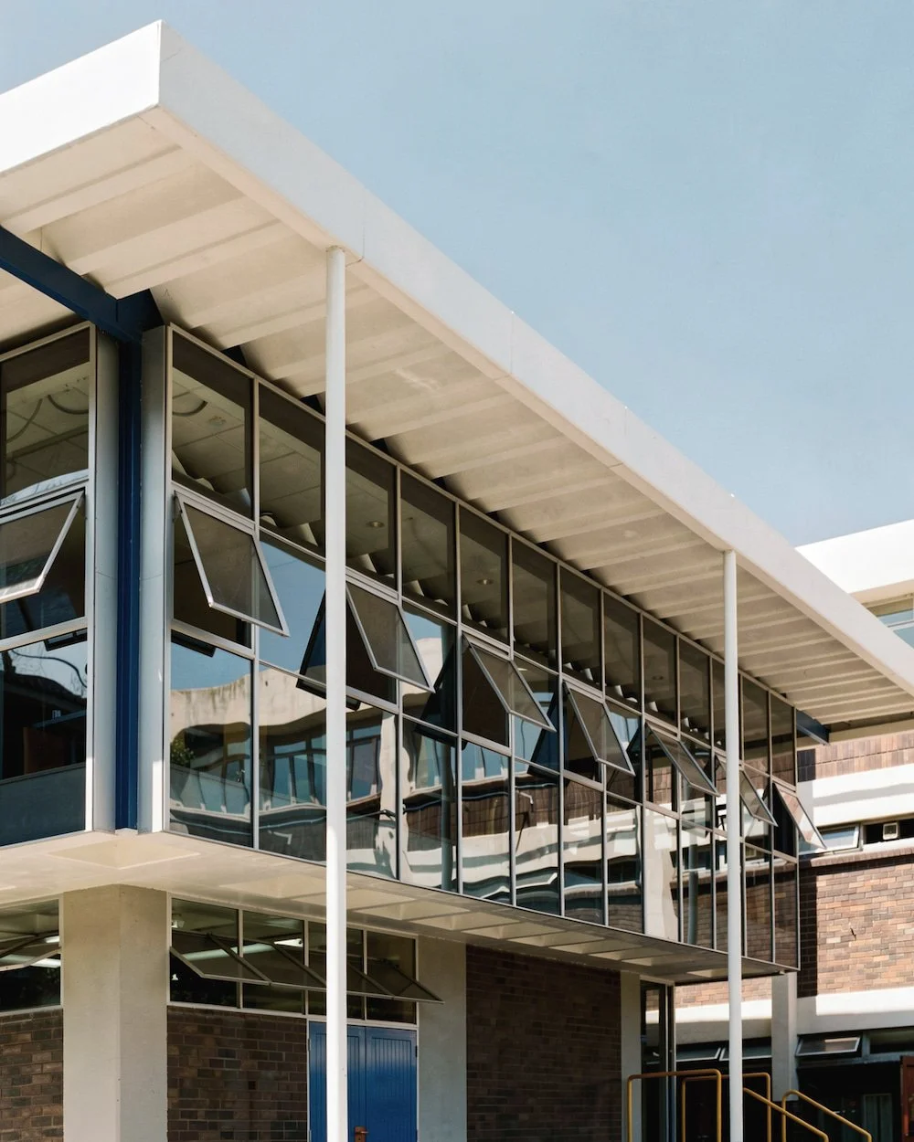 Modern building with large glass windows and exterior awnings, steel poles, and brick wall.