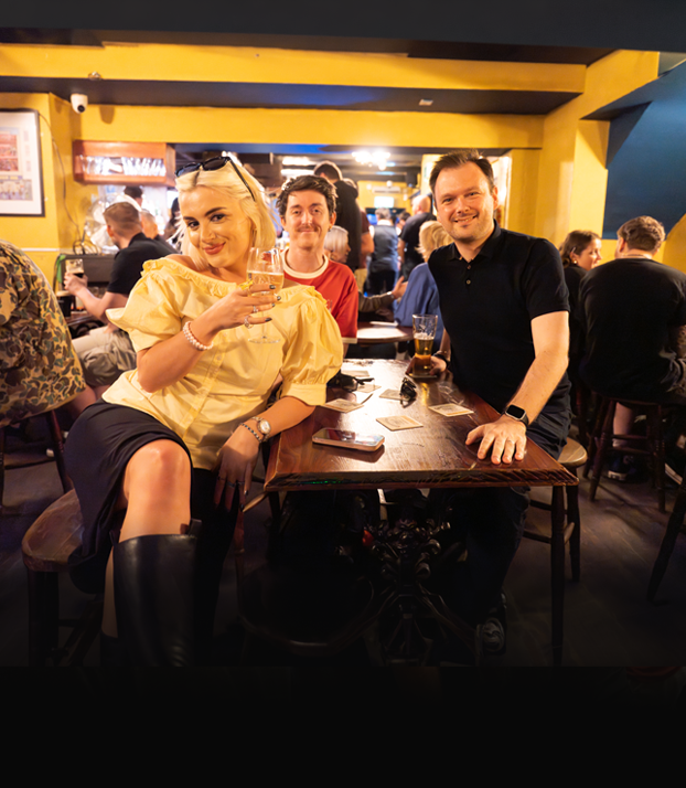 Group of people sitting at a bar table in a lively pub, enjoying drinks and socializing.