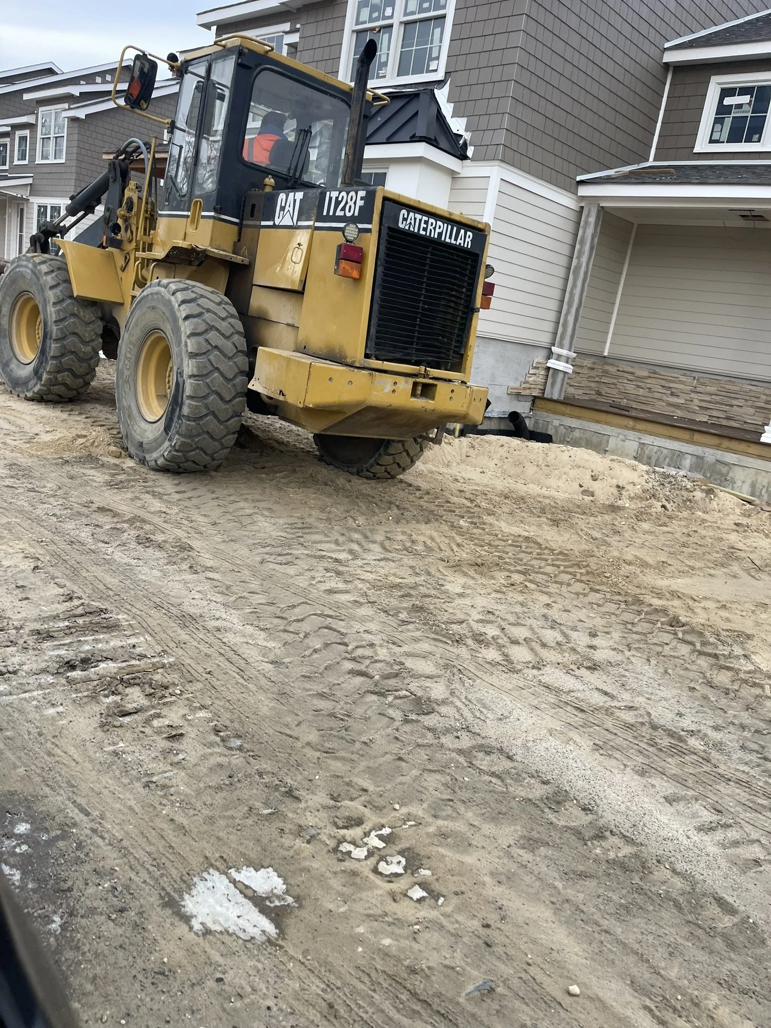 A yellow Caterpillar IT28F loader on dirt ground in front of a residential building with multiple stories and windows.