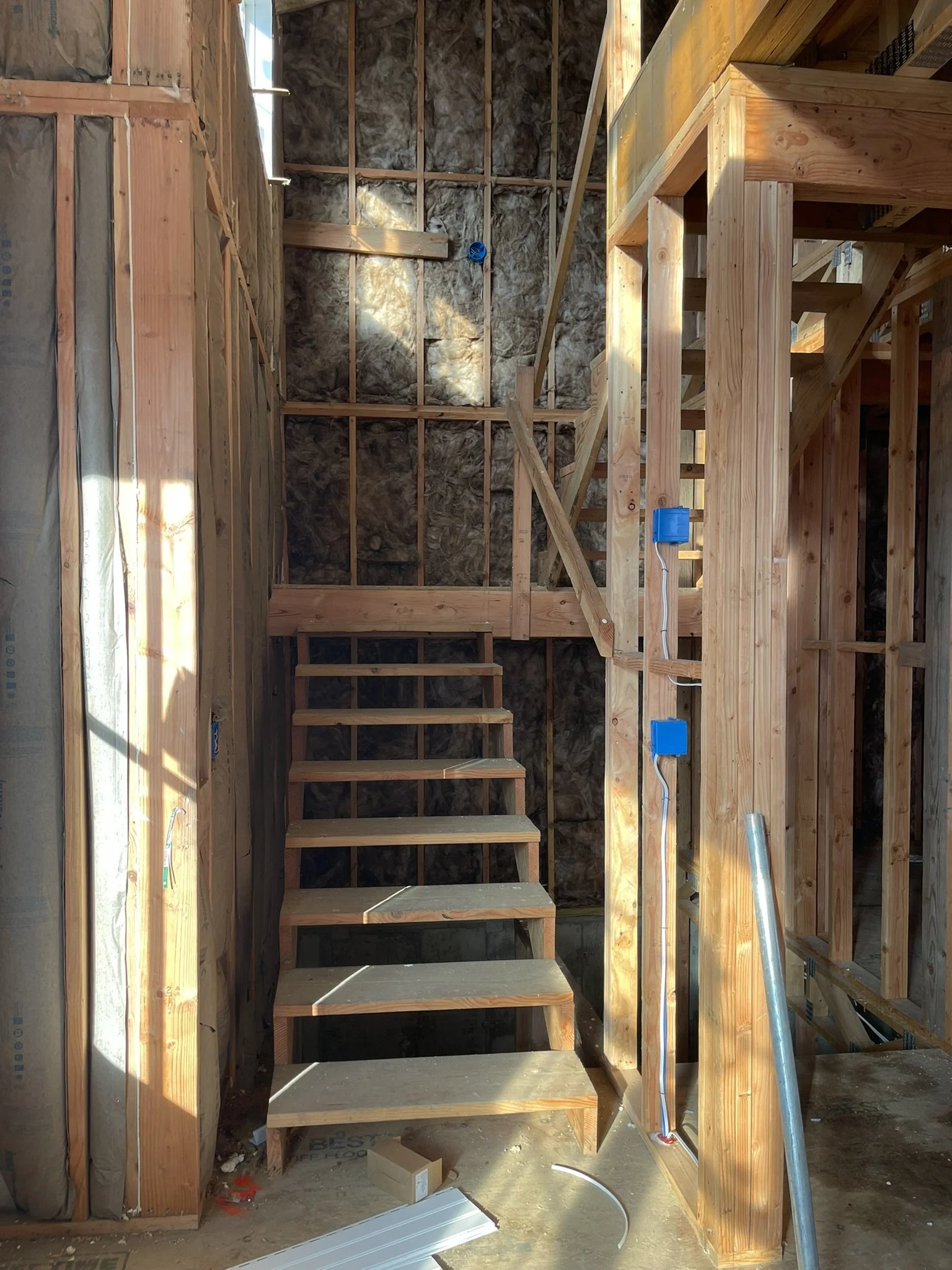 Interior of a building under construction showing exposed wooden framing, stairs, and insulation on the walls.