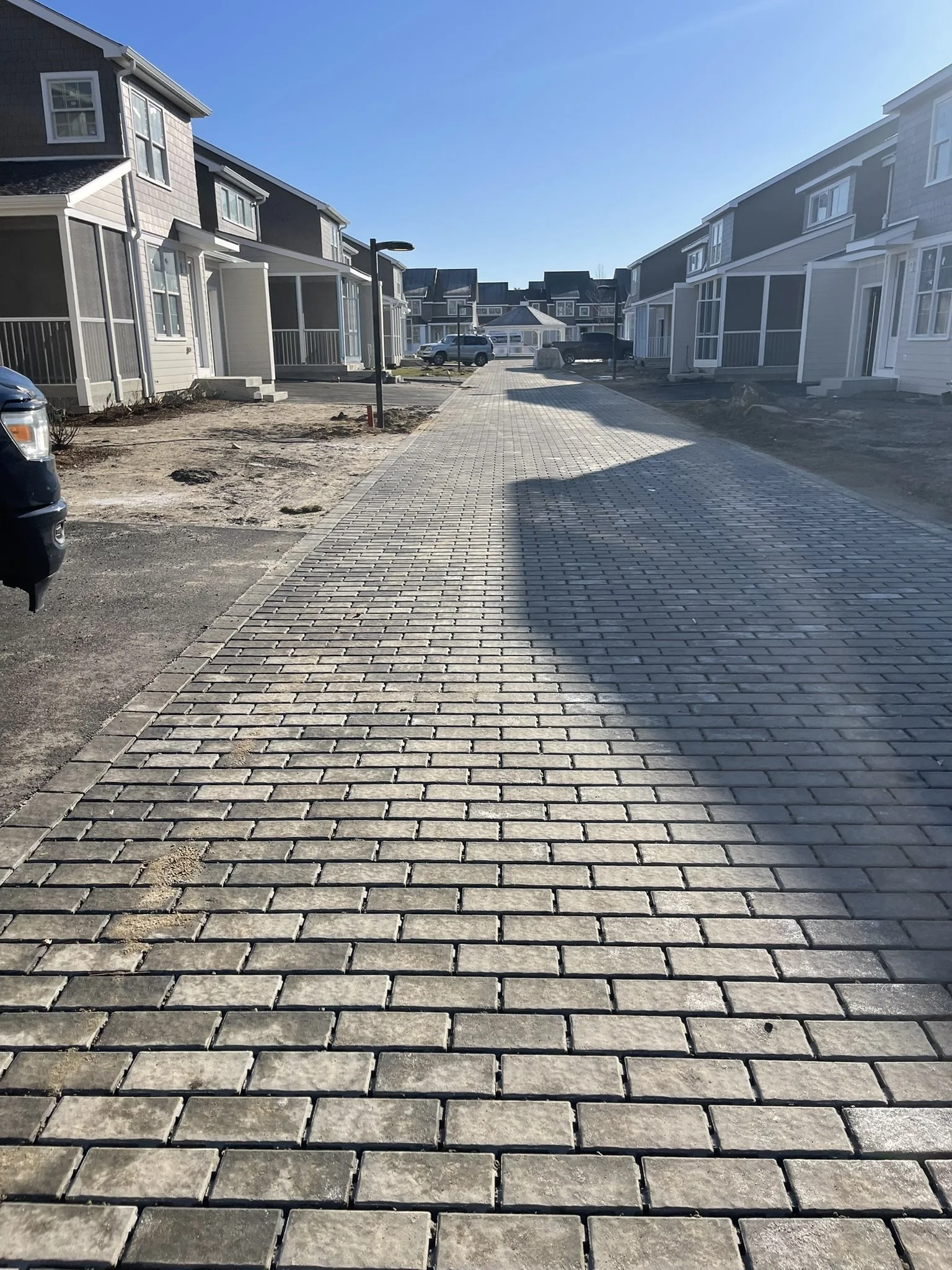 A paved walkway in a residential neighborhood with modern townhouse-style homes on either side and a clear blue sky overhead.