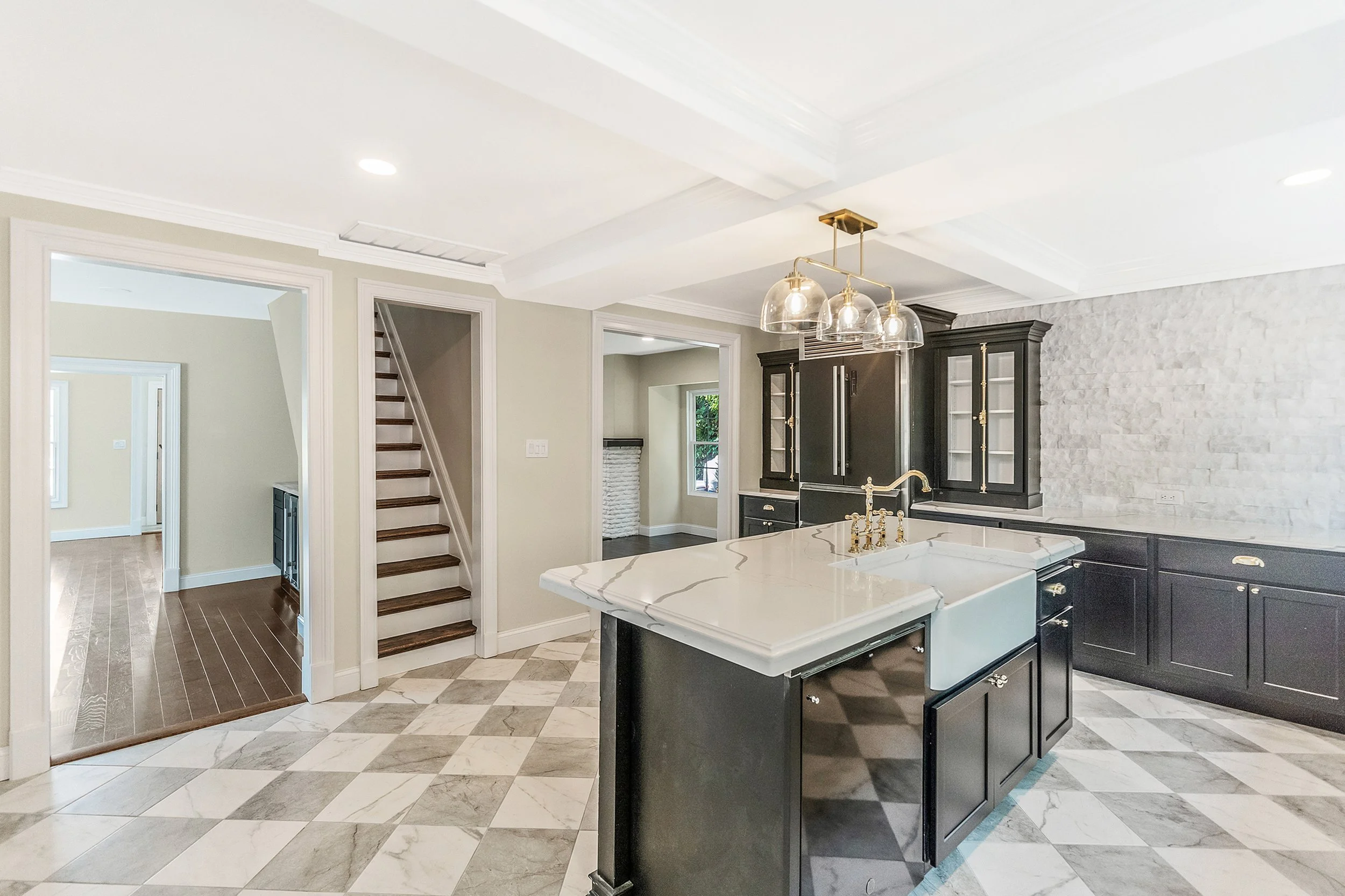 Modern kitchen renovation with custom black cabinetry, Calacatta quartz countertops, island seating, and gold chandelier by Shore Craft Contracting