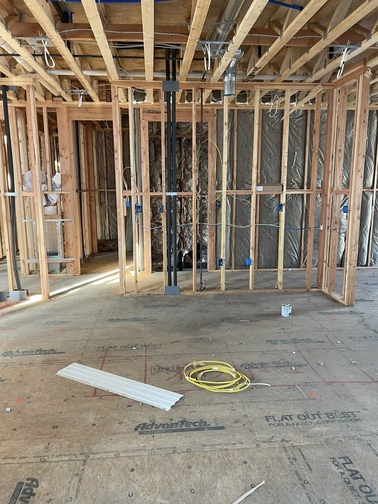 Interior of a building under construction showing exposed wooden framing, steel ductwork, electrical wiring, and worksite materials on the unfinished floor.