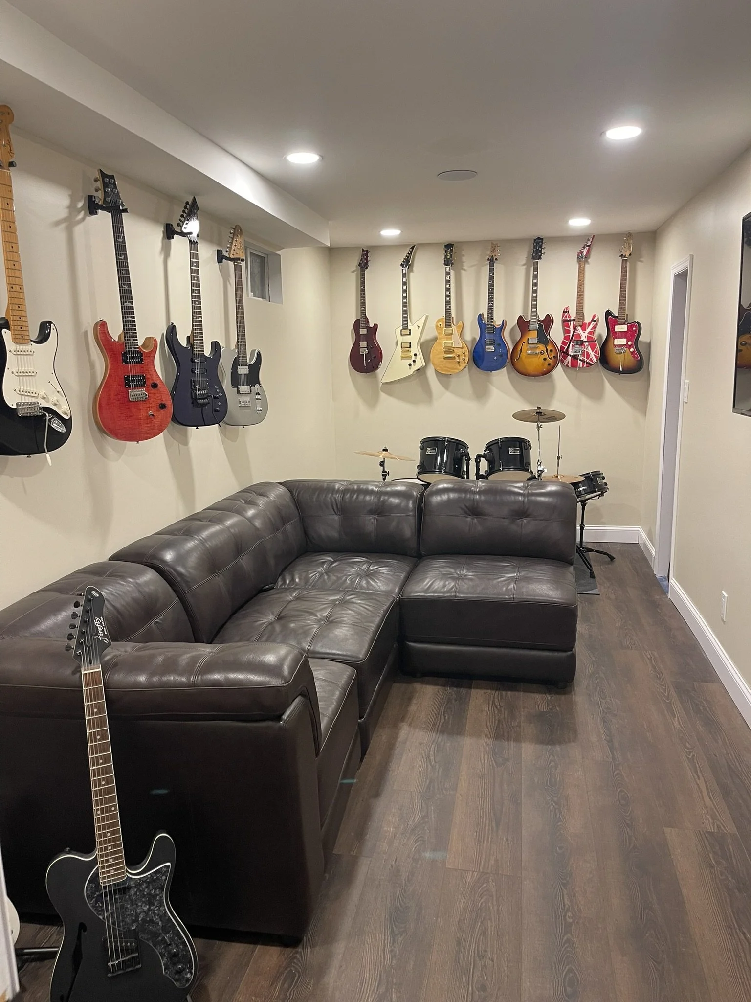 Finished recreation room with custom interior finishes, wall-mounted guitars, sectional seating, and music area