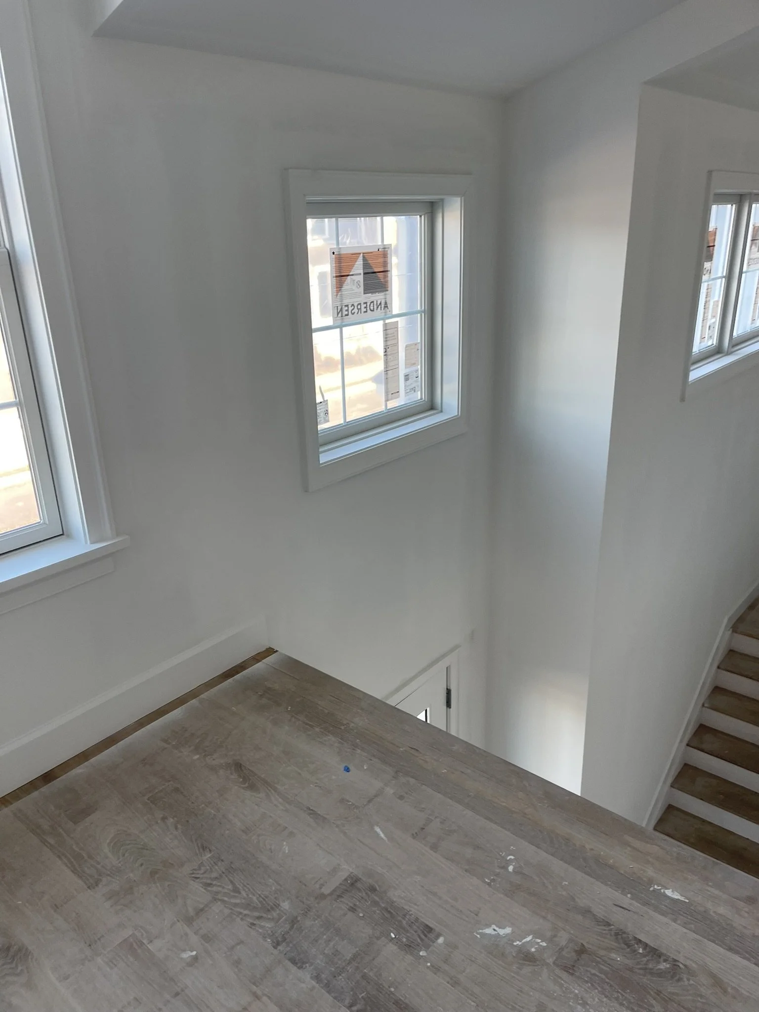 Interior view of a house with white walls, hardwood floors, and multiple windows, showing a staircase on the right side.