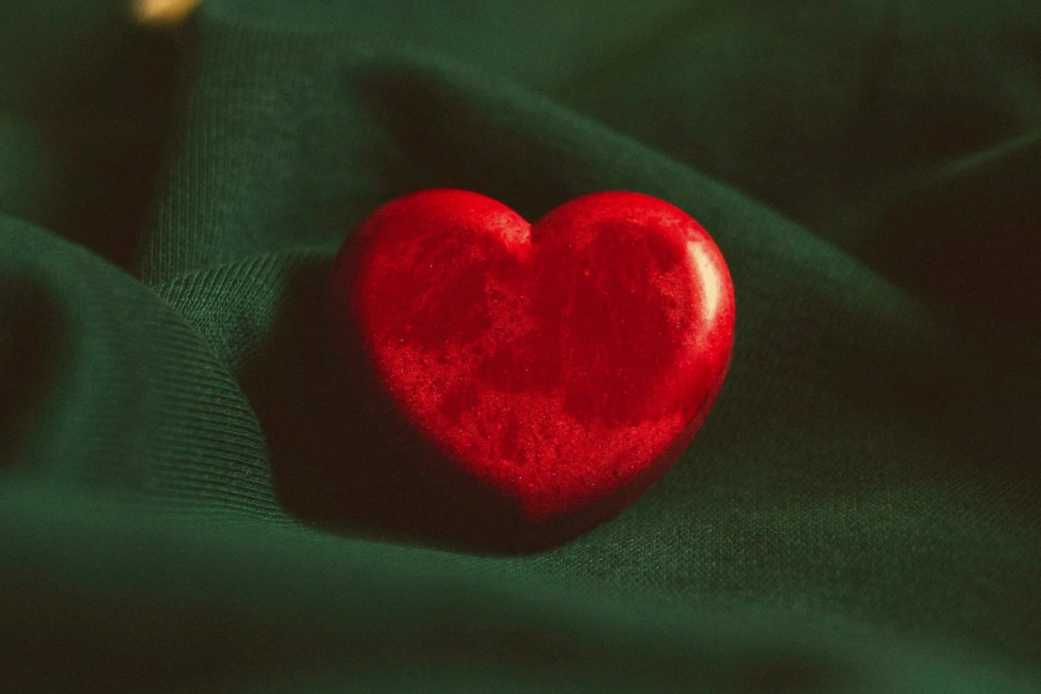 A red heart-shaped stone resting on dark green fabric.