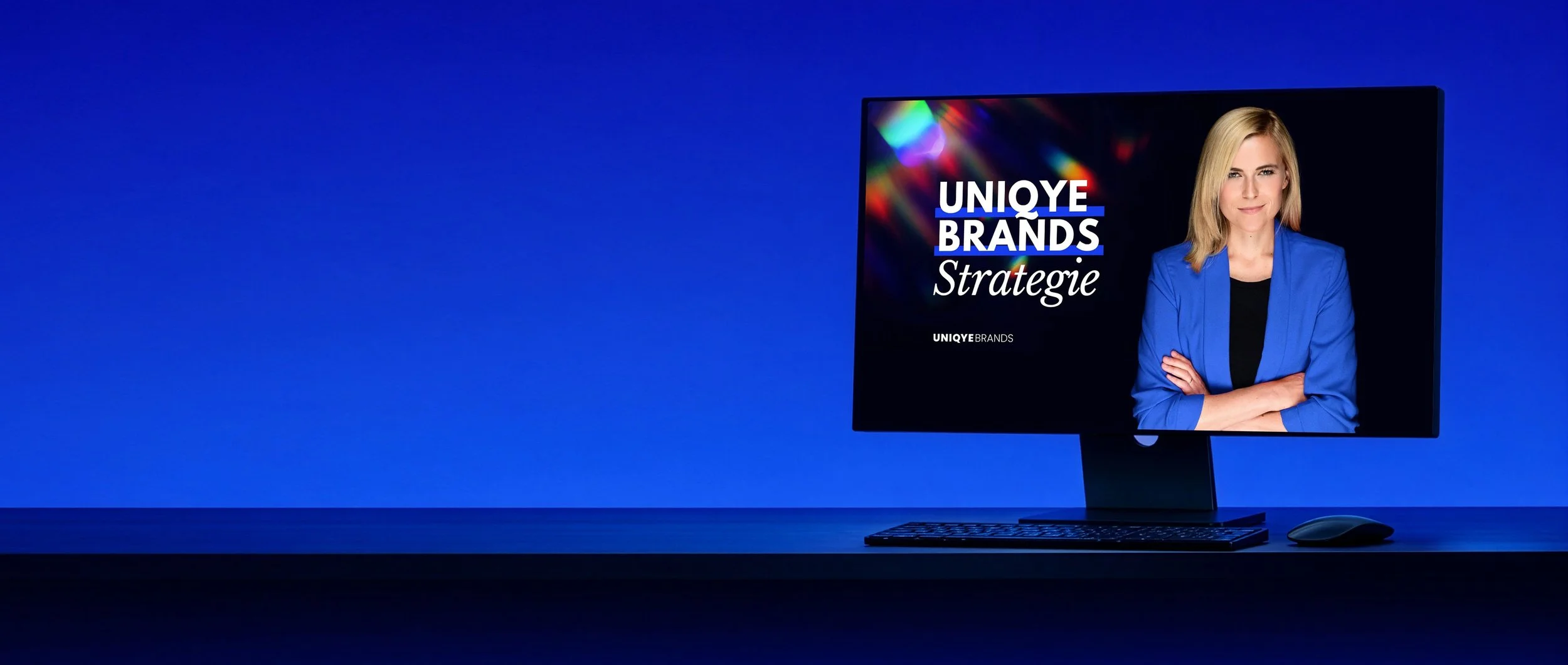 Computerbildschirm mit einer Frau in blauer Jacke, daneben tastatur und maus, im Hintergrund ein blauer Hintergrund, Schrift auf dem Bildschirm: "UNIQUE BRANDS Strategie".