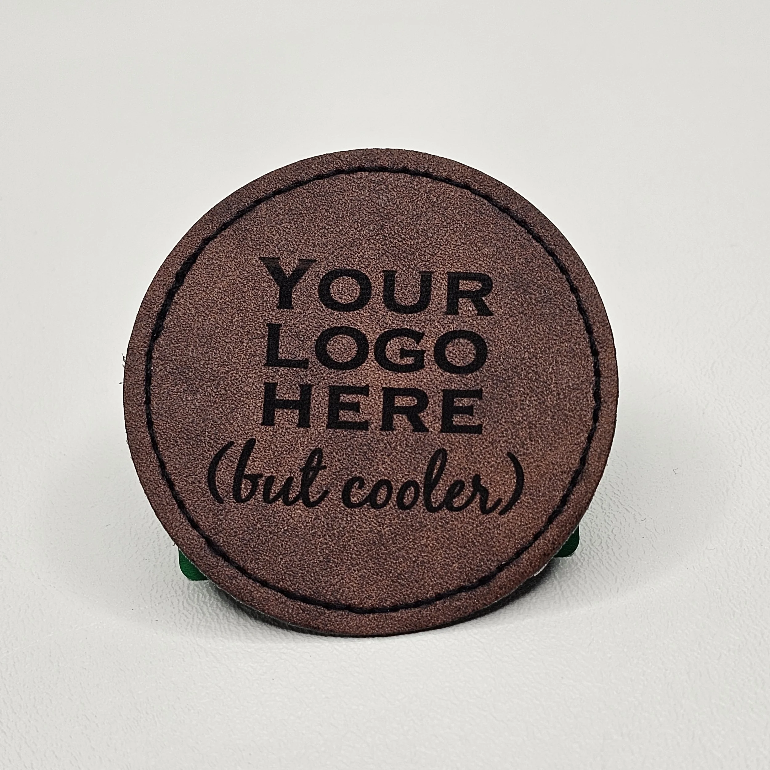 Round leather patch with the text 'Your logo here (but cooler)' printed in black on a white background.