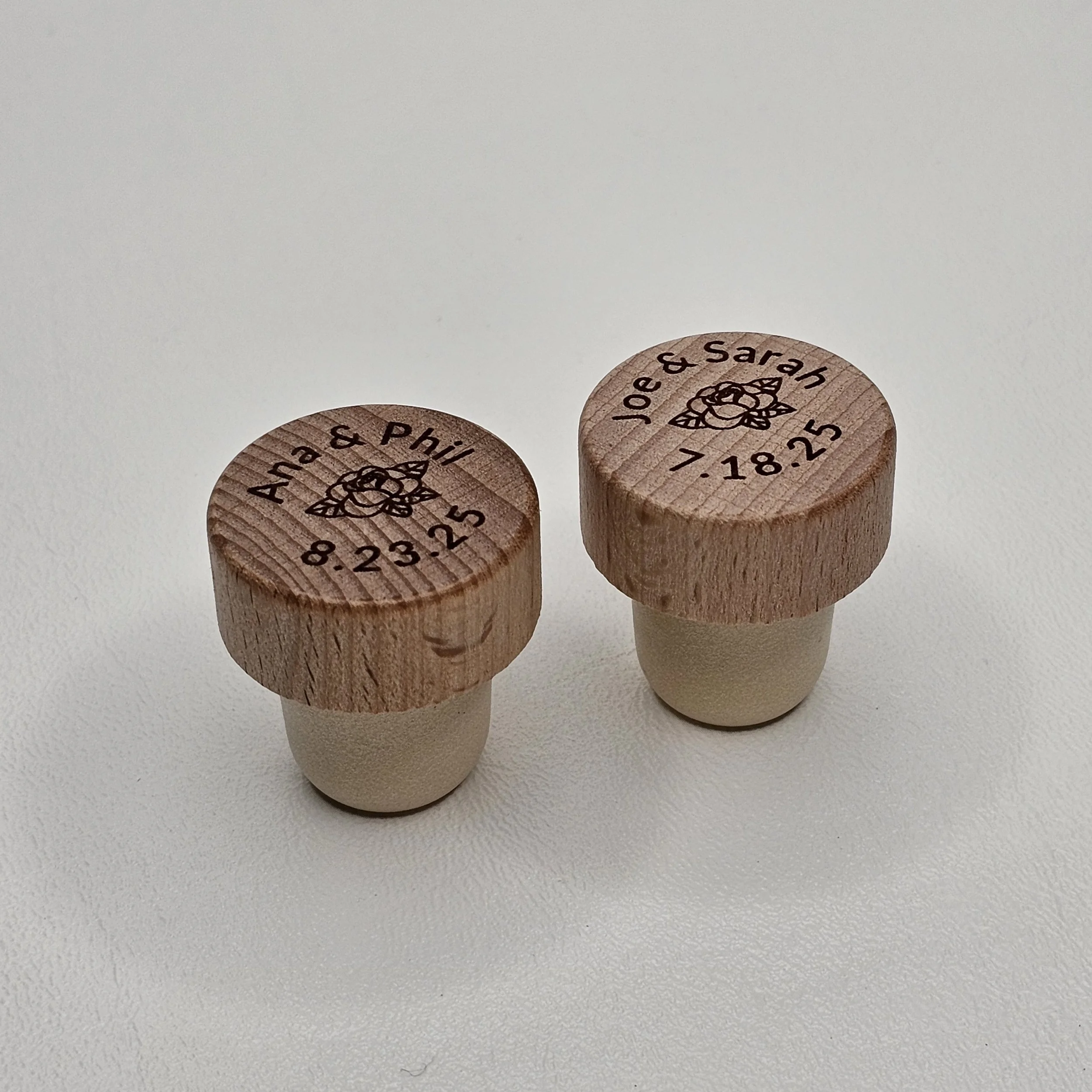 Two custom engraved golf tee markers with names and dates, 'Aha & Phil 9.23.25' and 'Joe & Sarah 7.18.25', placed on a plain white surface.