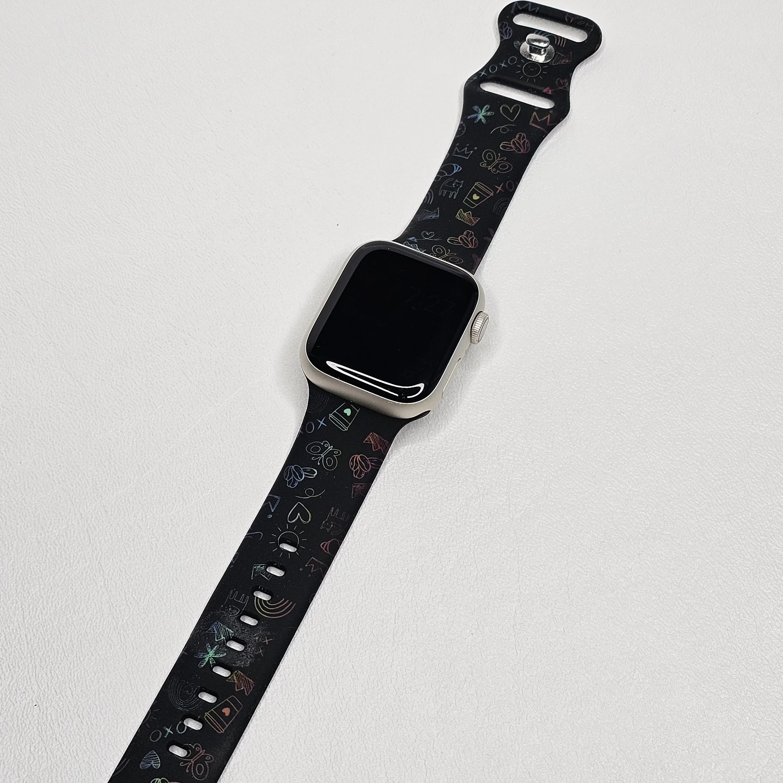 Smartwatch with a black band and colorful doodle patterns on a white surface.