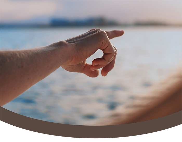 A person pointing with their hand towards a blurry body of water in the background.