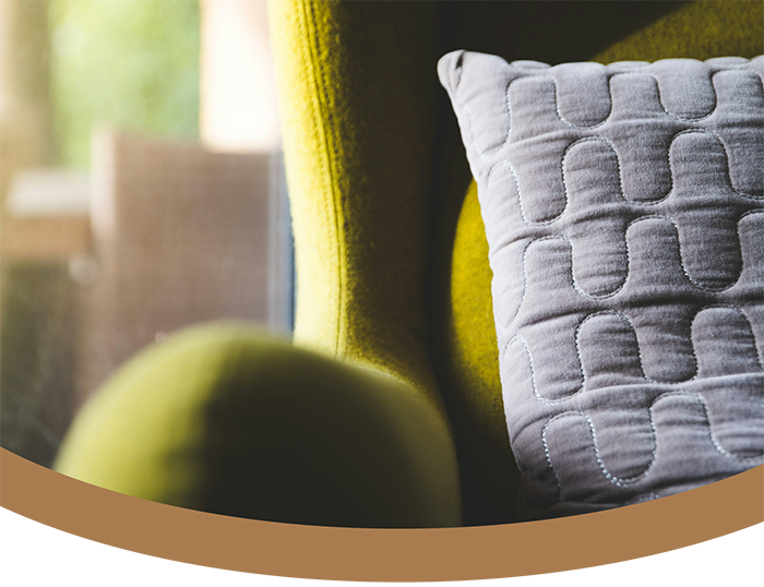 Close-up of a green upholstered armchair with a gray decorative pillow on it, in a sunlit room.