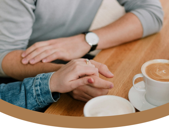 A couple holding hands on a wooden table with coffee cups.