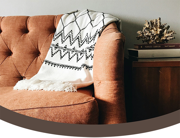 A coral upholstered sofa with a white and black patterned throw blanket draped over the backrest, next to a wooden side table with a small decorative coral sculpture and a stack of books.