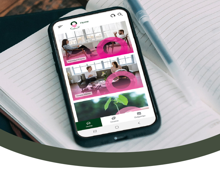 Smartphone displaying a home cleaning app with images of women cleaning and a plant, lying on an open notebook with a pen nearby.