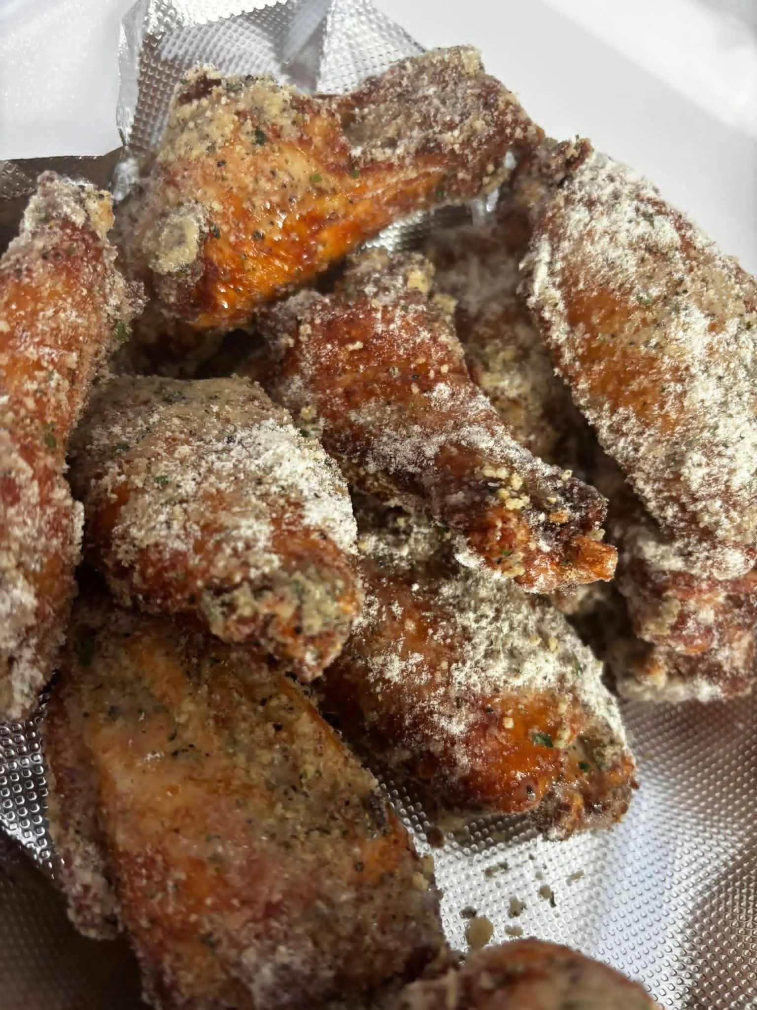 Fried chicken wings coated with seasoning and spices, lying in a metal strainer.