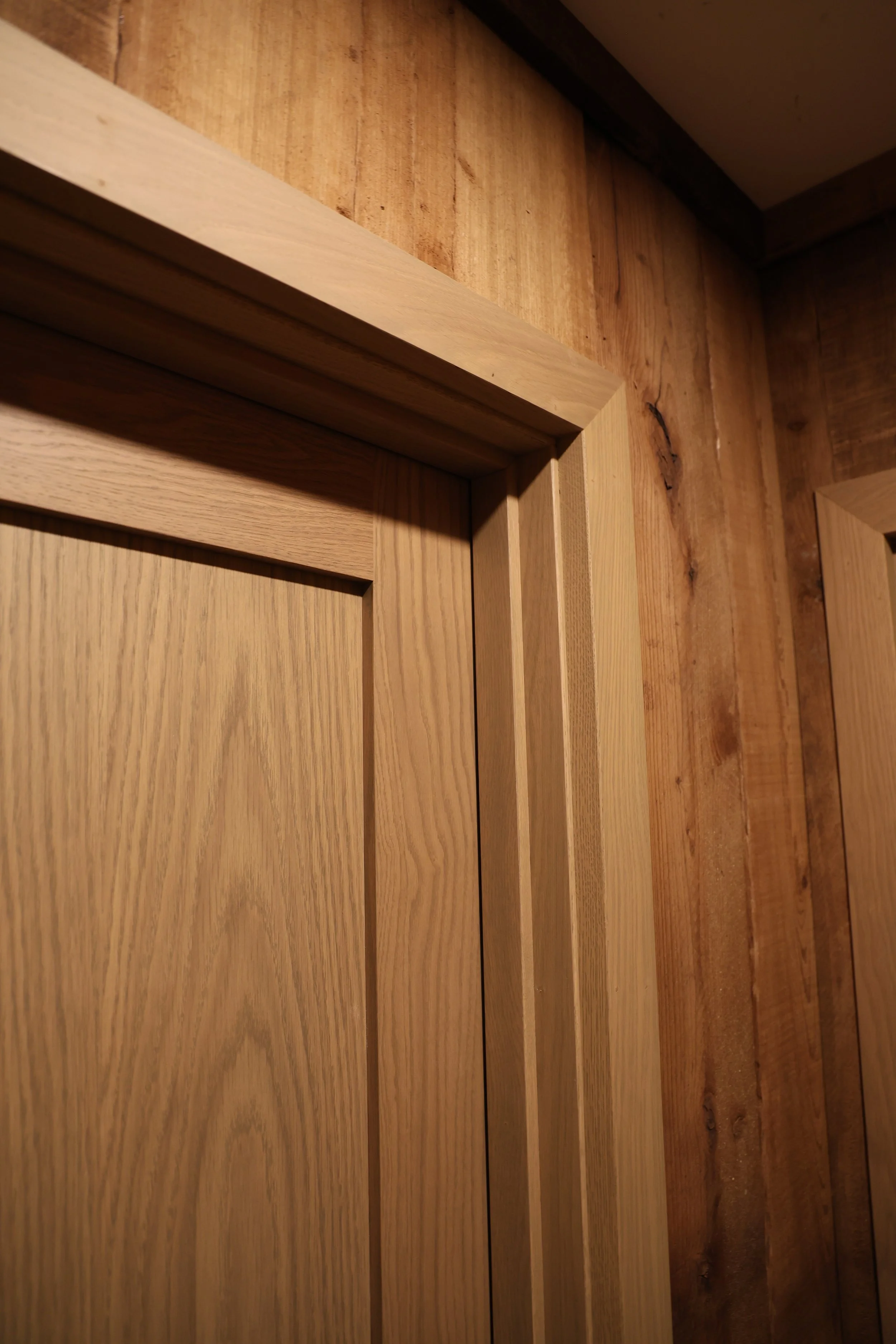Close-up of a wooden door frame and paneling with natural wood grain and knots, against a darker wooden wall.