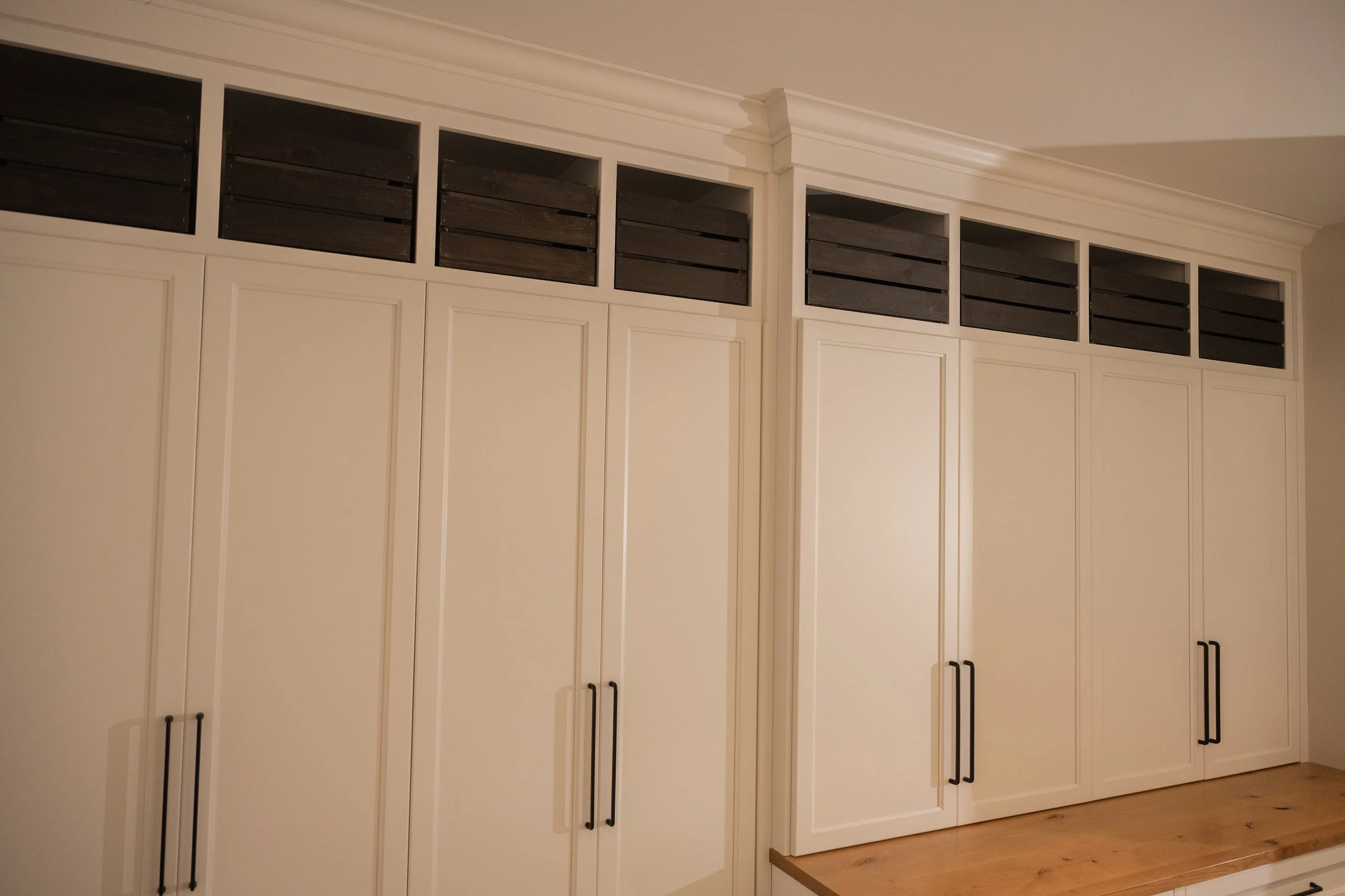 Closet with white cabinets and black handles, featuring ventilated dark wood panels at the top.