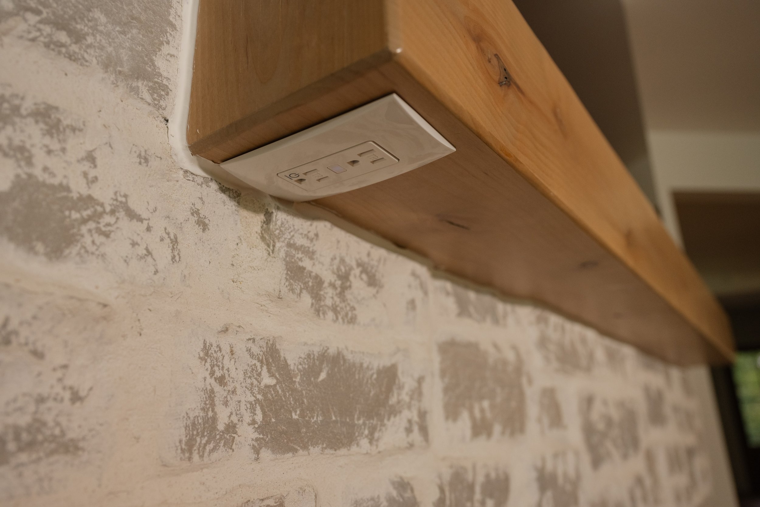 Electrical outlet mounted on a wooden surface next to unfinished, textured wall.