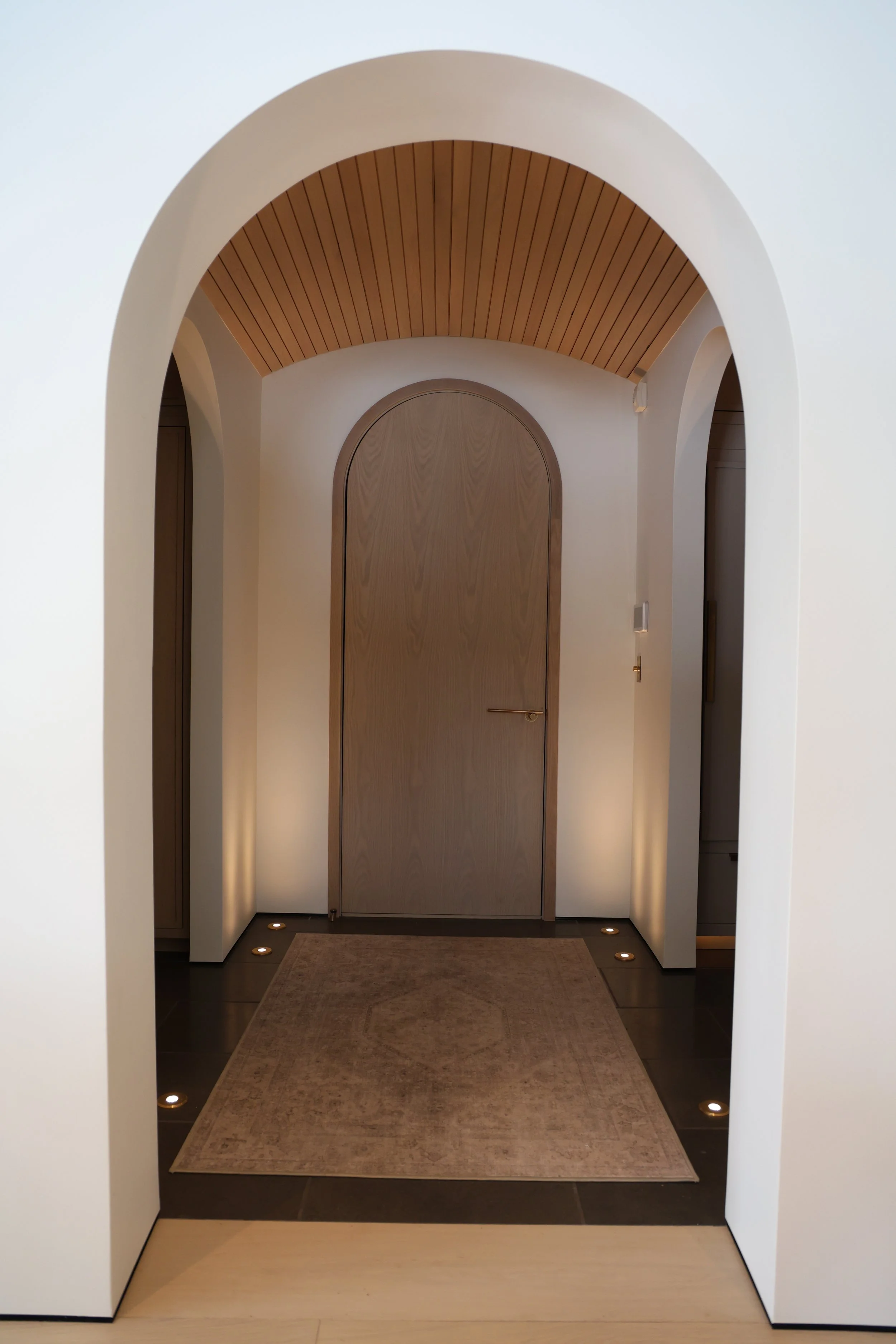 Interior view of a hallway with arched doorways, wooden ceiling, beige carpet, and small recessed lights on the floor.