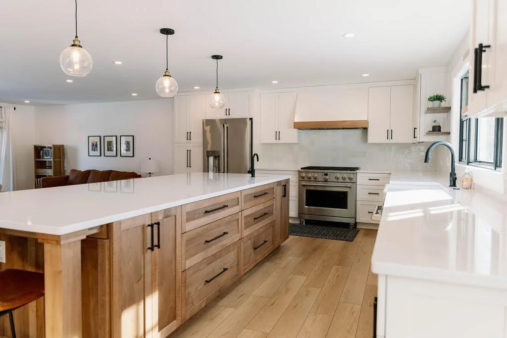 Modern kitchen with white cabinets, wooden island, stainless steel appliances, pendant lights, and large windows.