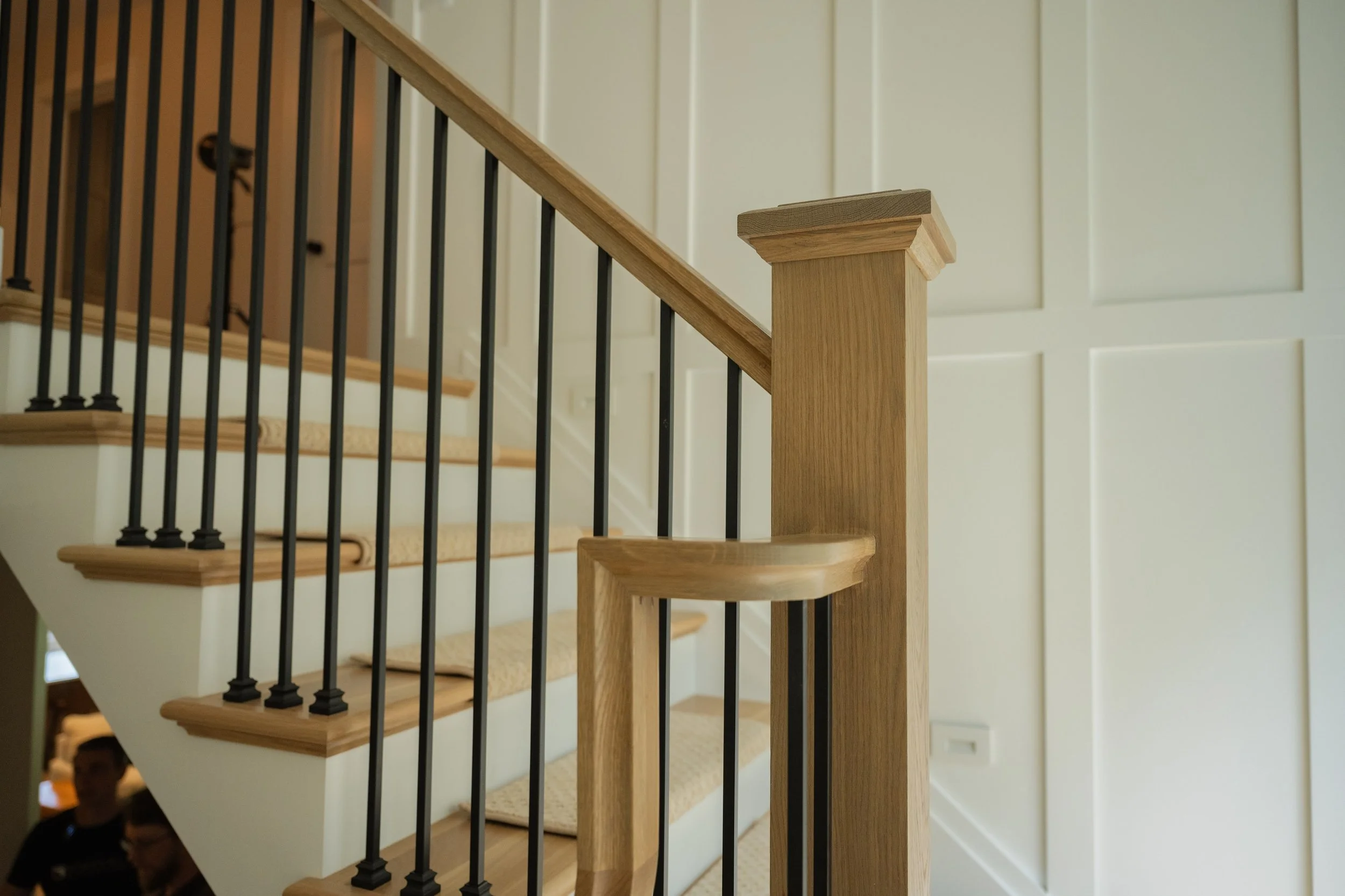 A close-up of a stair railing with a wooden post and black metal balusters in a modern home interior.