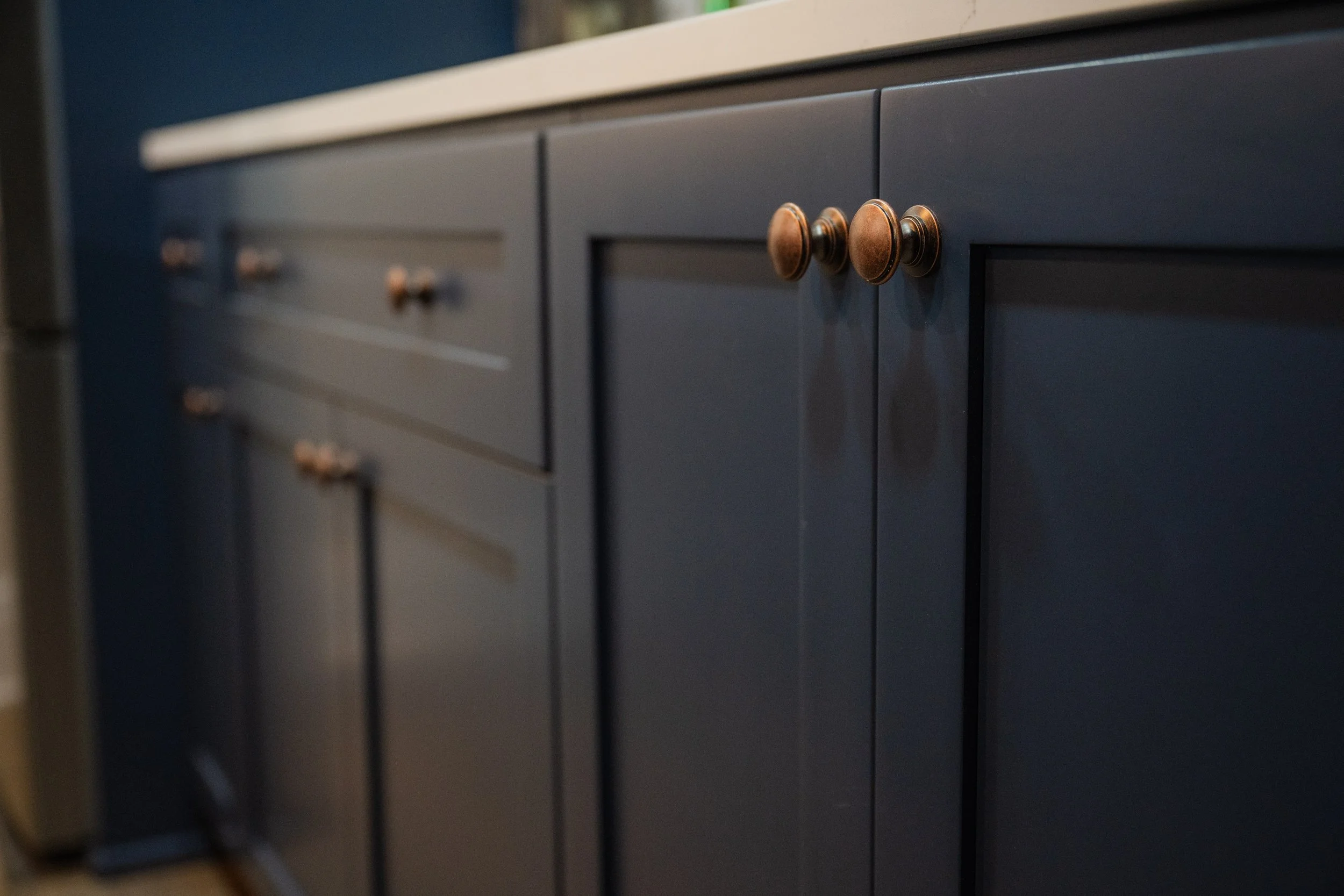 Close-up of a dark blue custom cabinet with round, bronze-colored knobs on the doors.