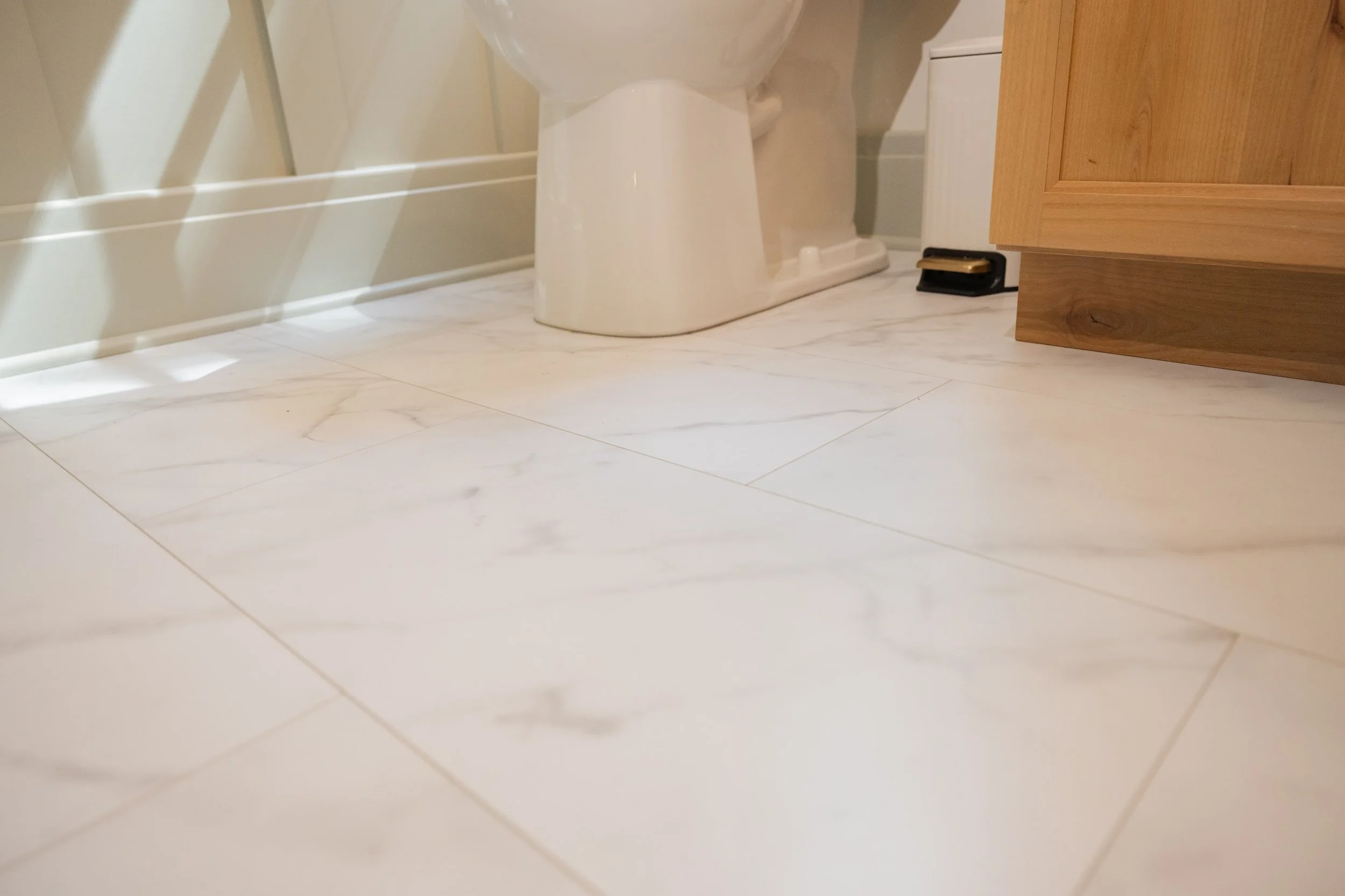 A bathroom with white marble floor tiles, a white toilet, and a wooden cabinet on the right side.