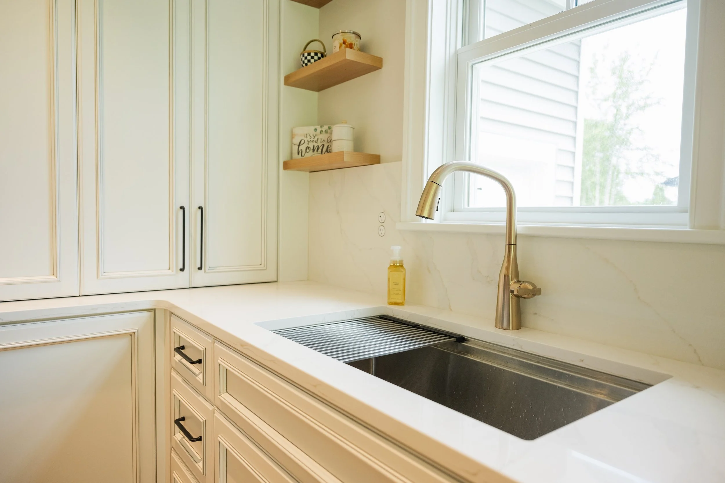 Kitchen with white cabinets, a marble countertop, a gold faucet, a window with blinds, and a soap dispenser.