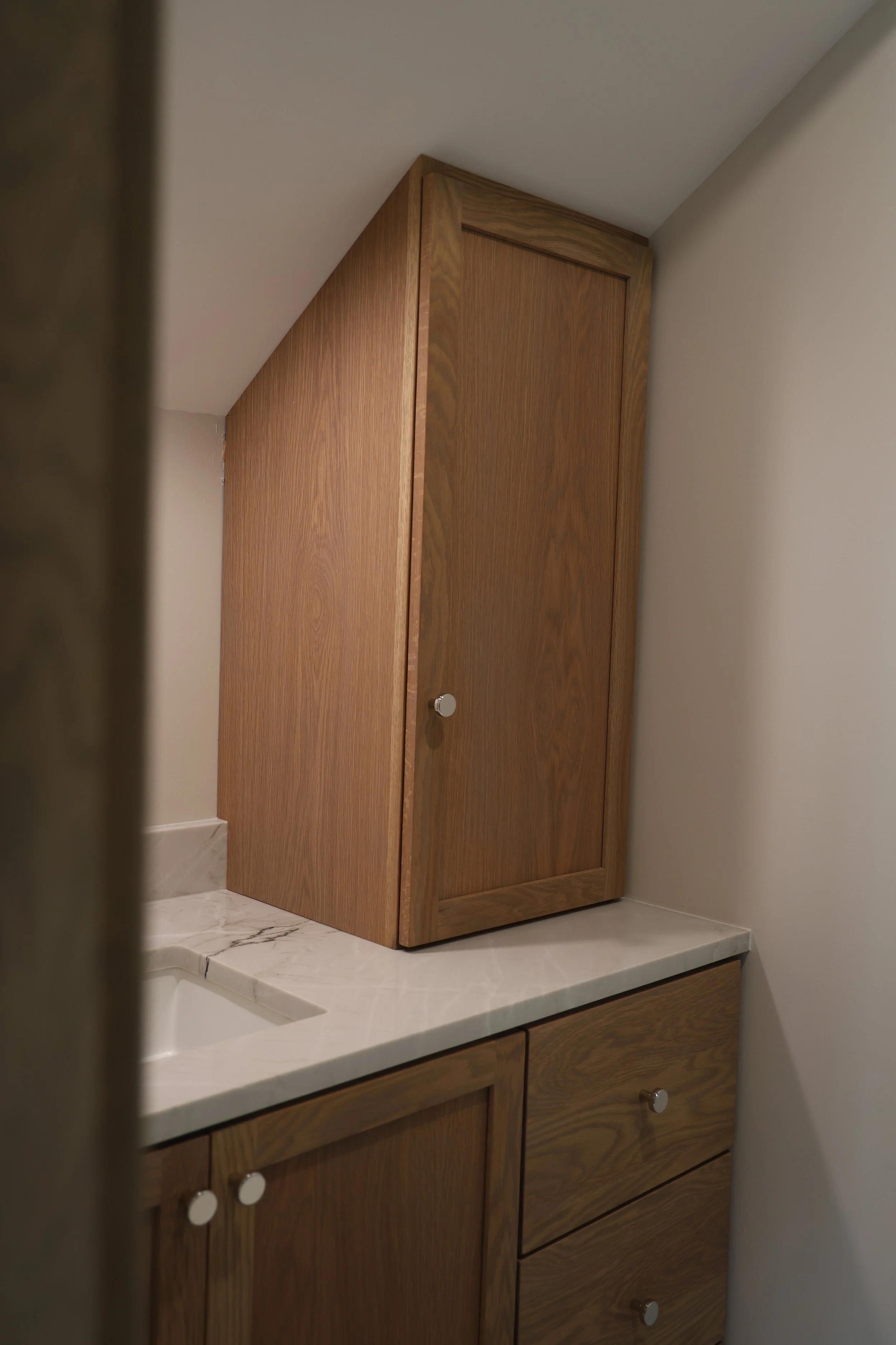A corner of a bathroom with a wooden cabinet above the sink and a marble countertop.